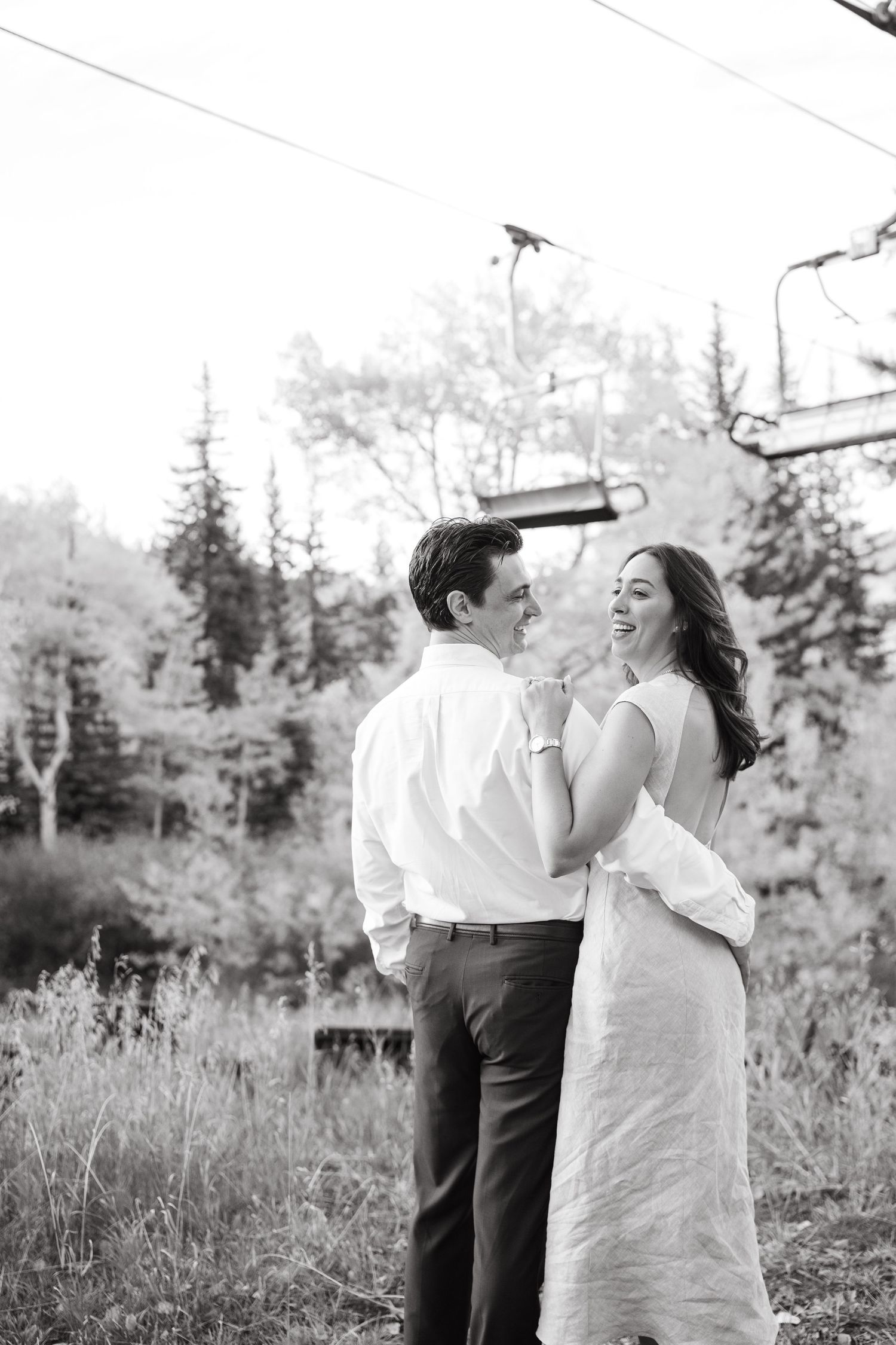 A romantic black and white photo of a couple laughing together in a mountain forest setting.