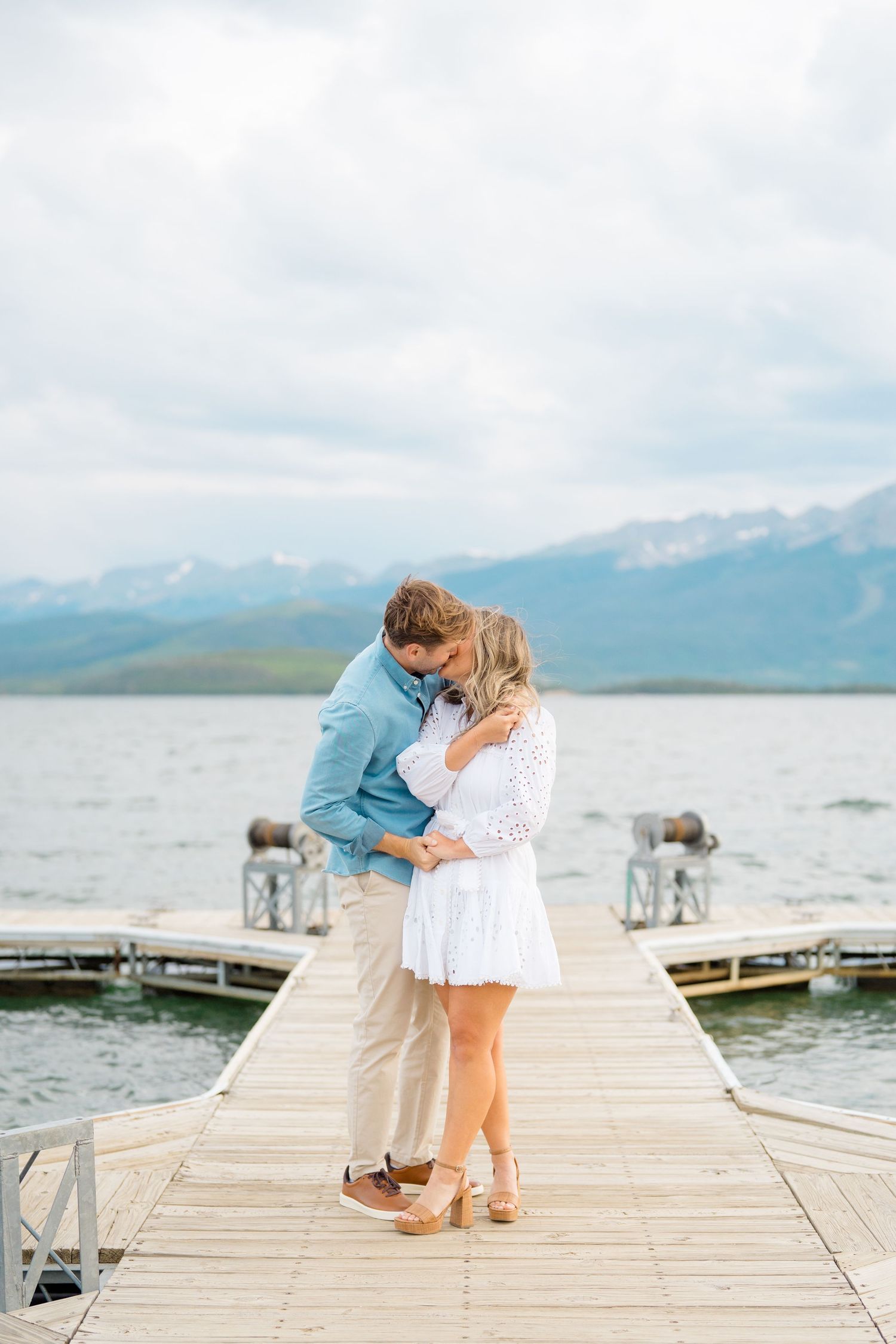 A couple embraces on a wooden dock overlooking a scenic mountain lake on a cloudy summer day at lake dillon.