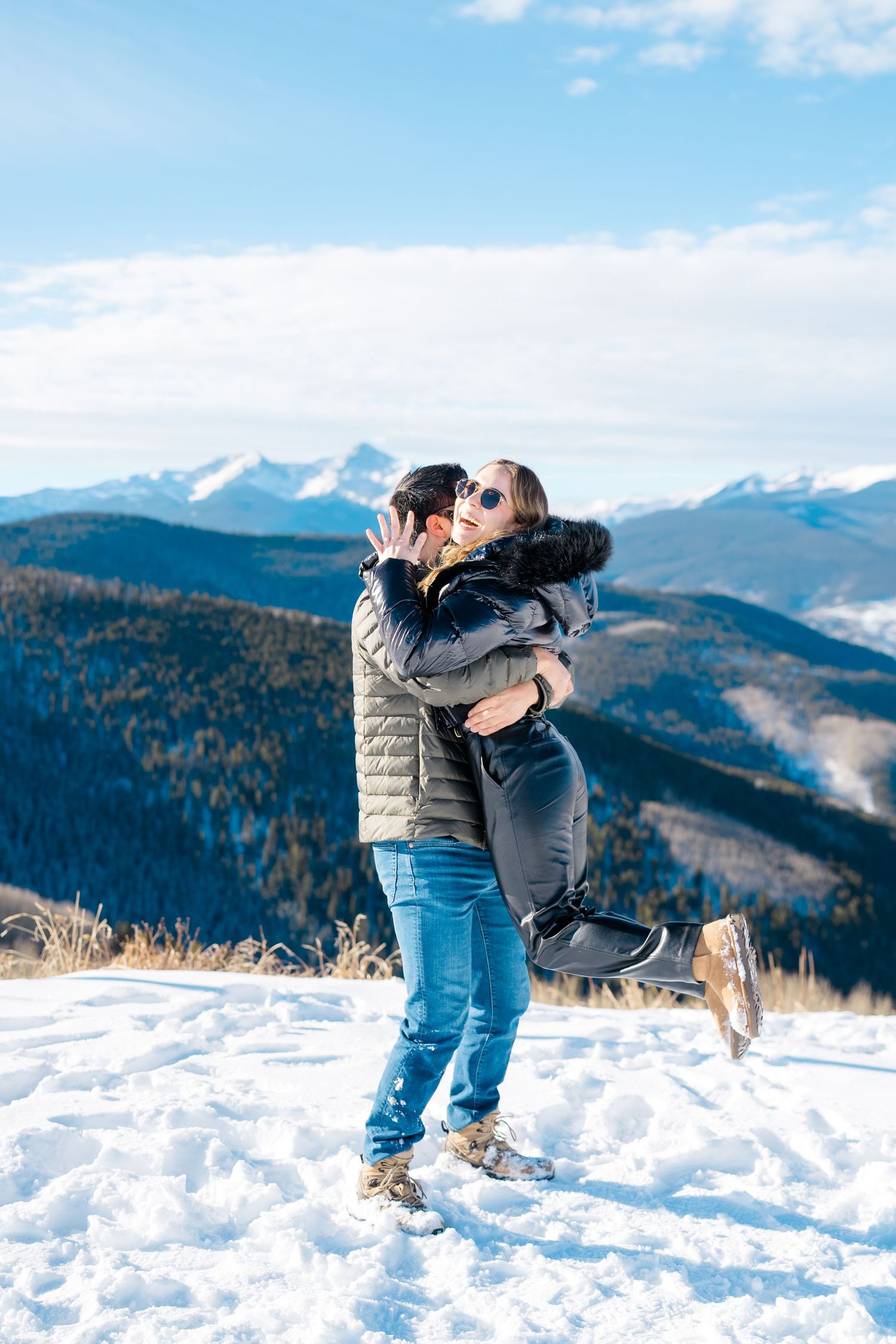 A couple embraces and shares a romantic moment in the snow with scenic mountain views in the background.