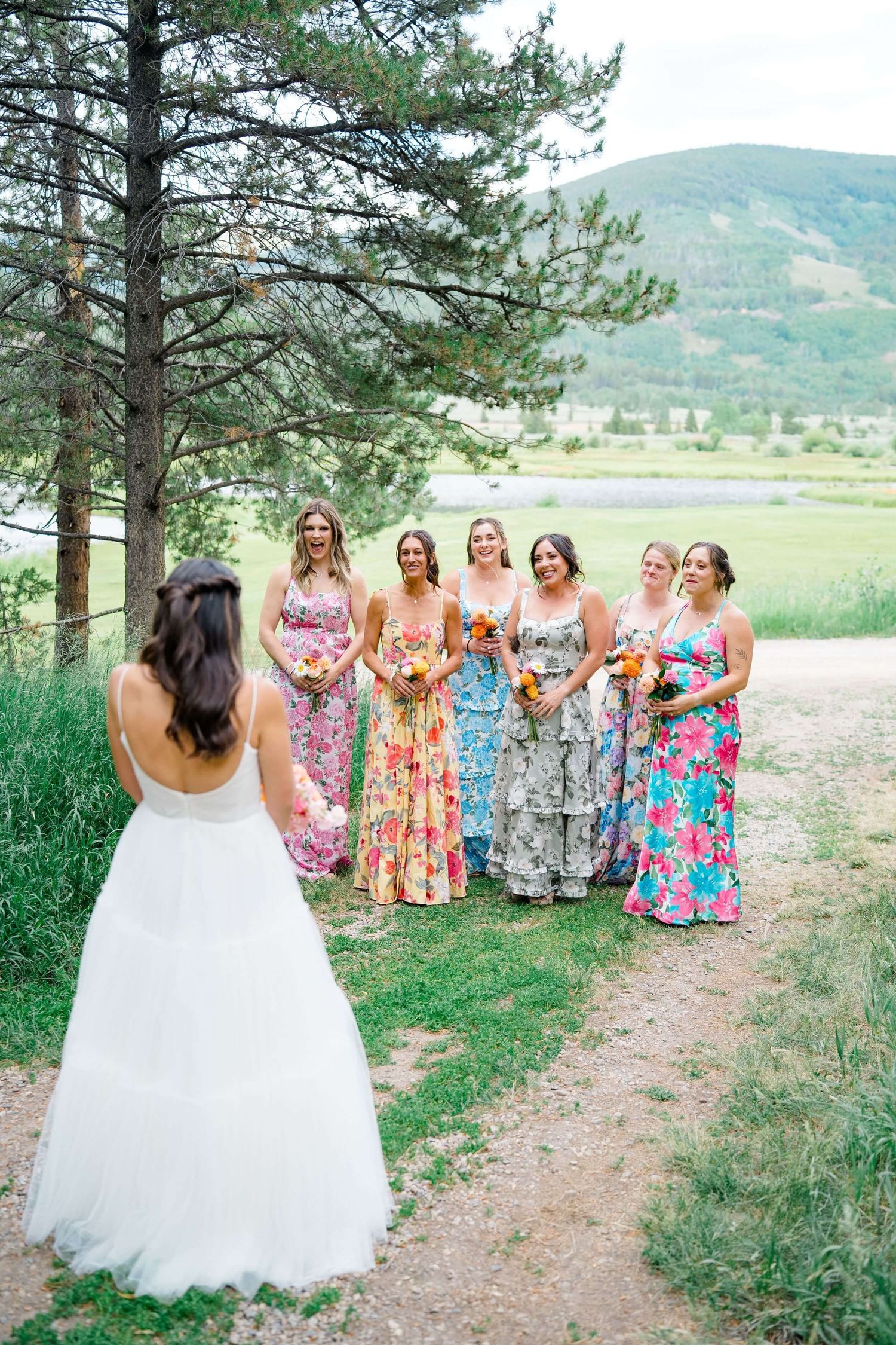 Camp Hale Wedding party in colorful floral dresses poses together in a mountain meadow with pine trees.