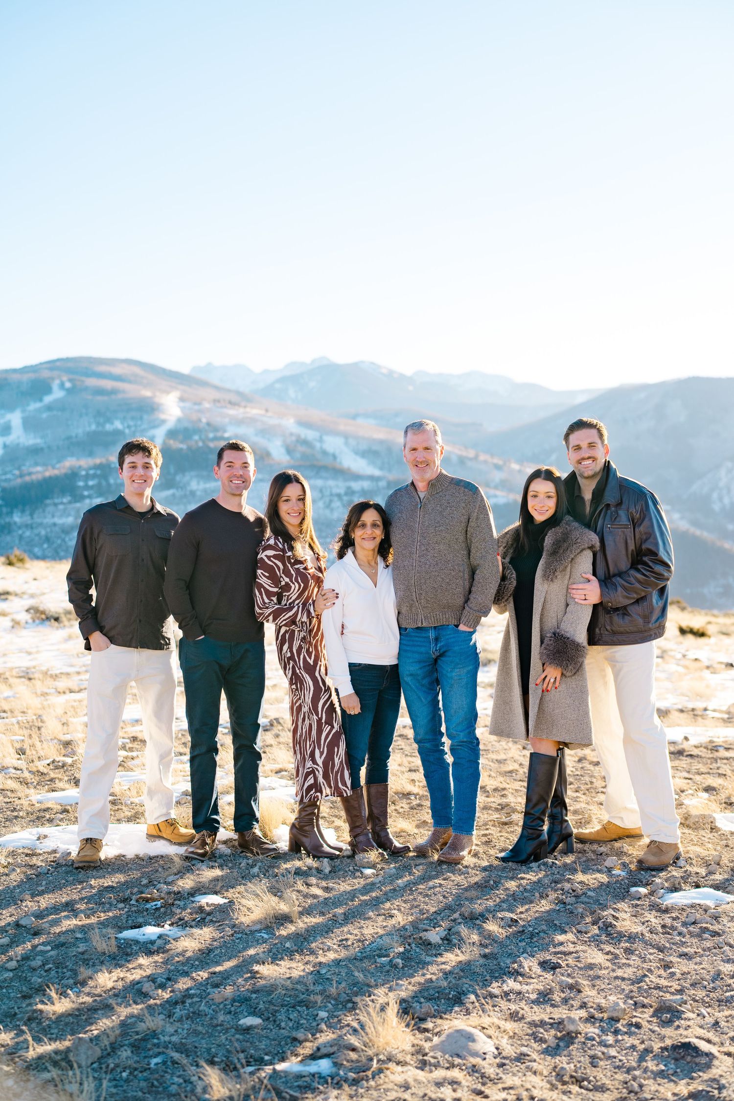 A group of people standing together on a mountain overlook with scenic hills in the background on a sunny day.