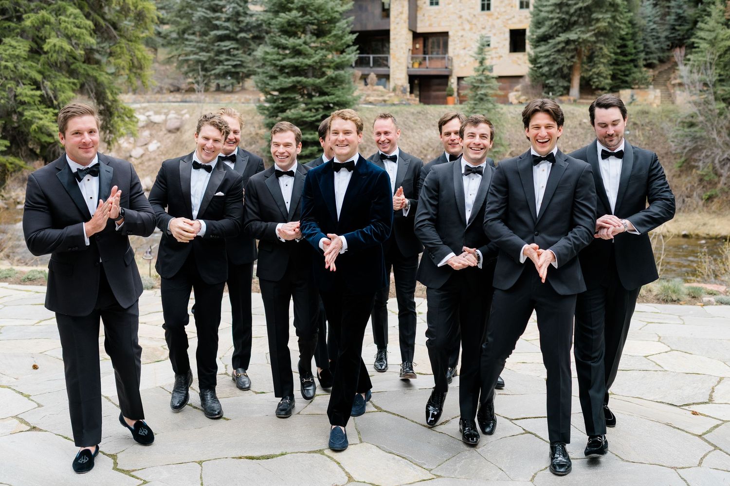 Groom and groomsmen in black tuxedos with bow ties laughing and walking together outdoors at a mountain wedding venue at Vail Sonnenalp Wedd