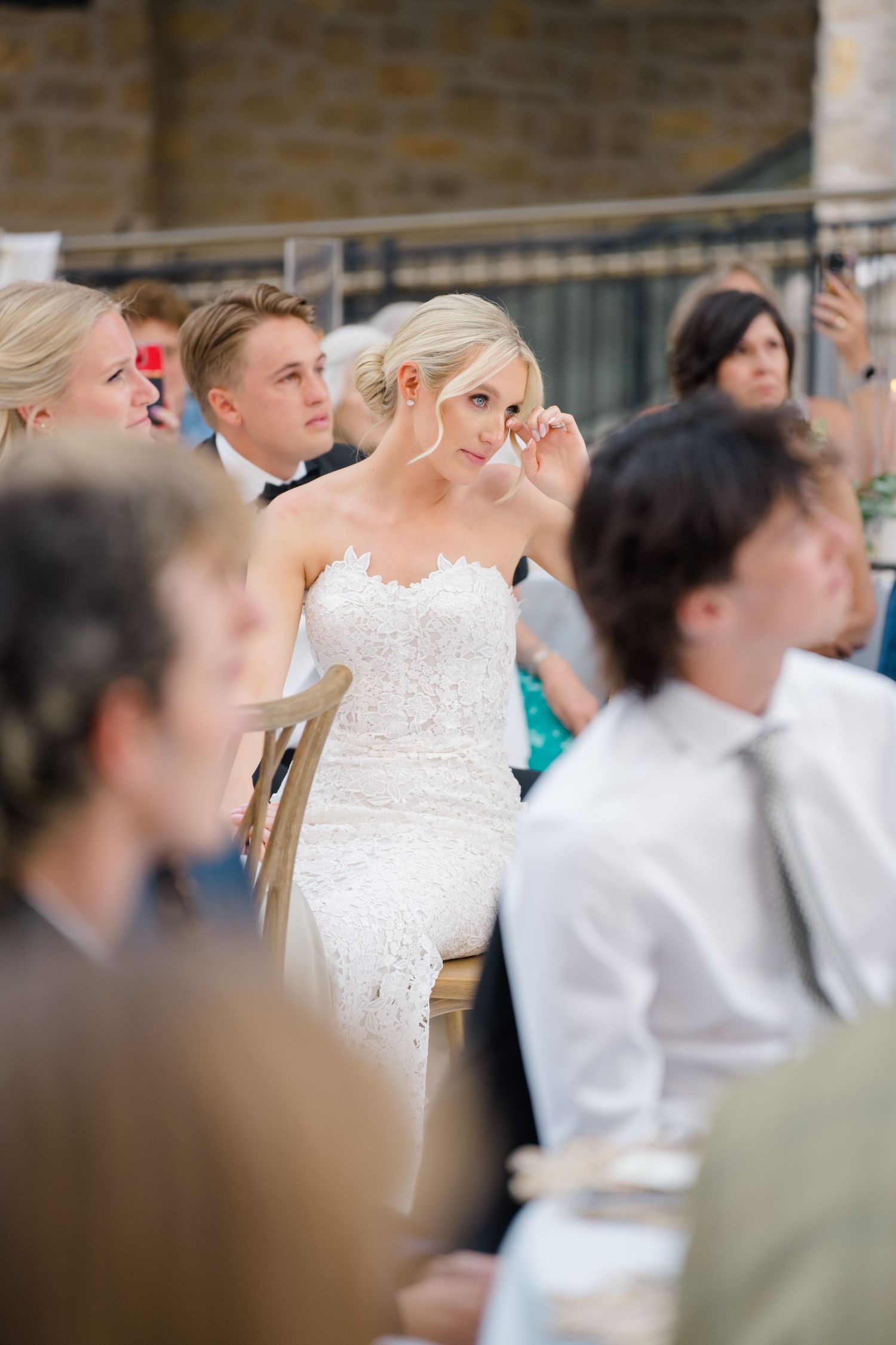 At Arrabelle Vail Wedding Emotional bride in white lace gown wiping tears at wedding reception surrounded by seated guests.