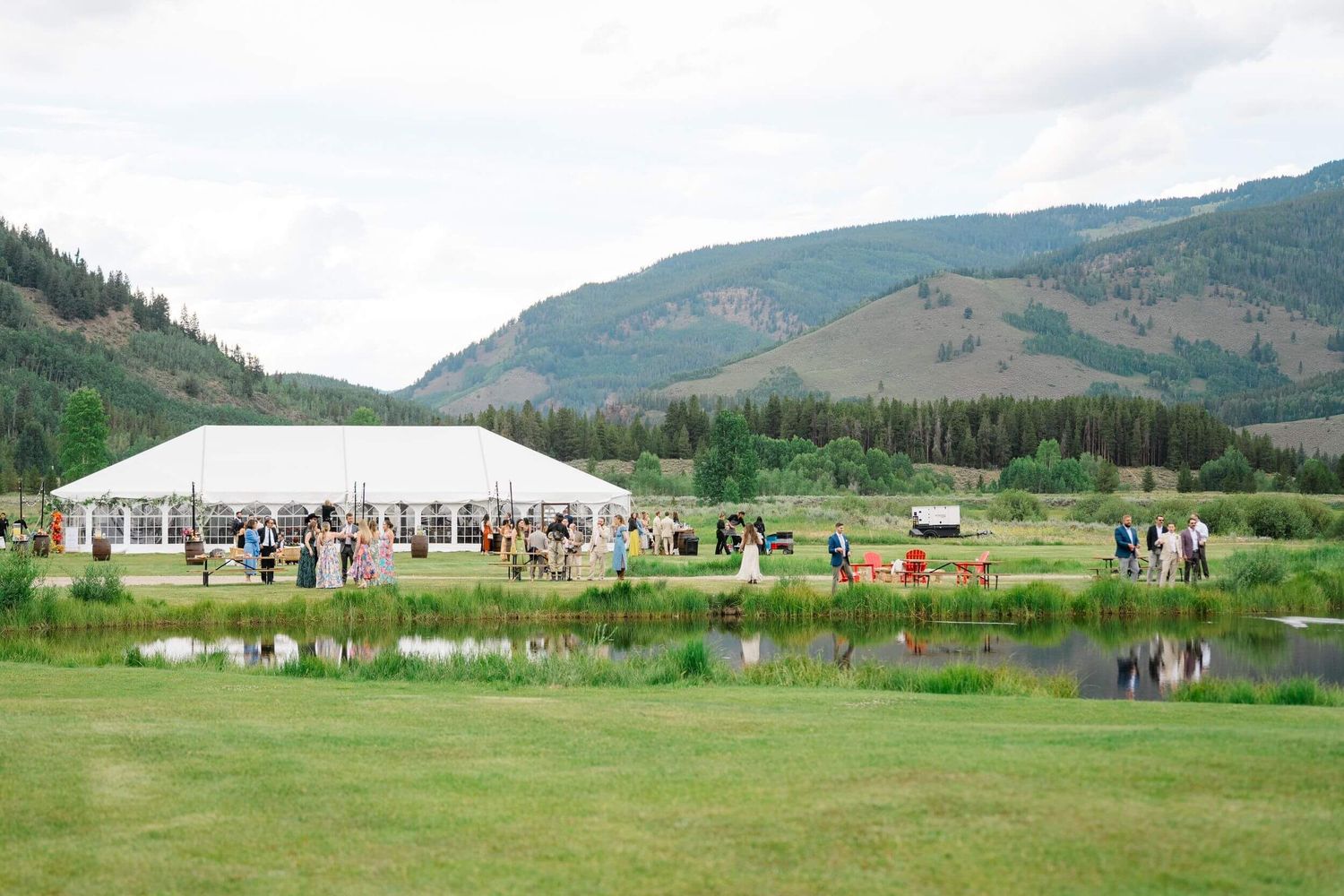 Camp Hale Venue - Panoramic view of a mountain wedding venue with white tents and guests gathered on a lush green lawn.