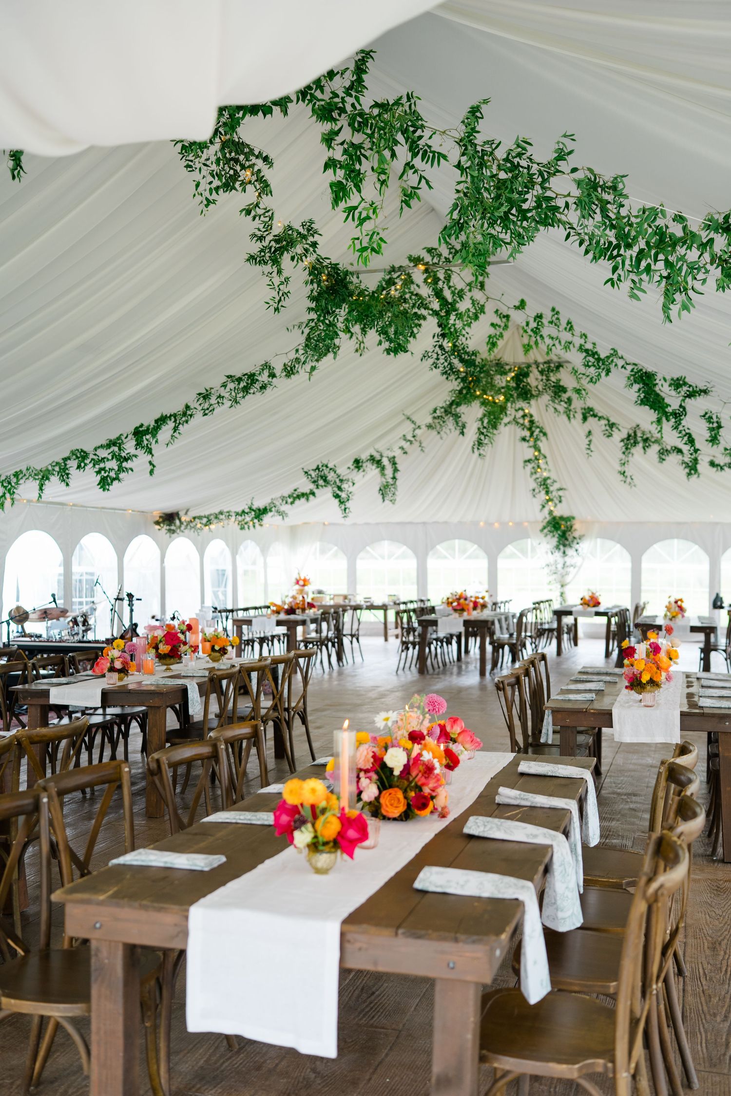 An elegant wedding reception tent with rustic wooden tables, white linens and greenery draped from the ceiling.