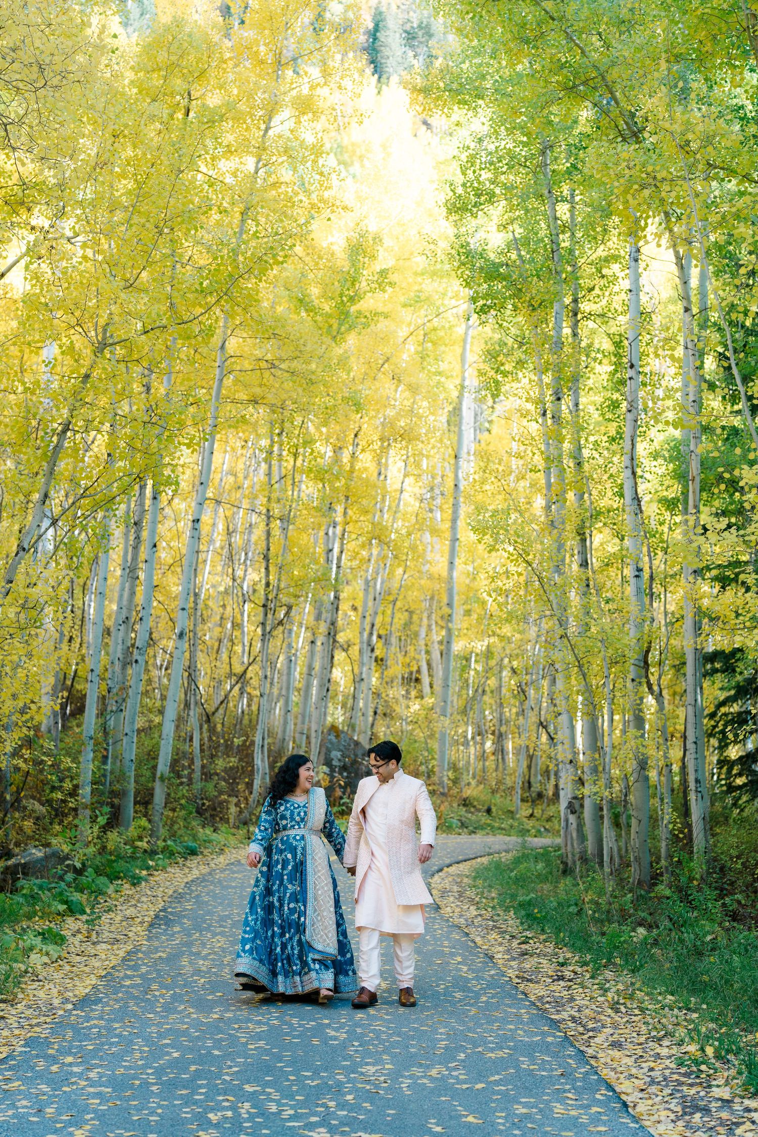 A couple walks down a scenic path surrounded by golden aspen trees on an autumn day.