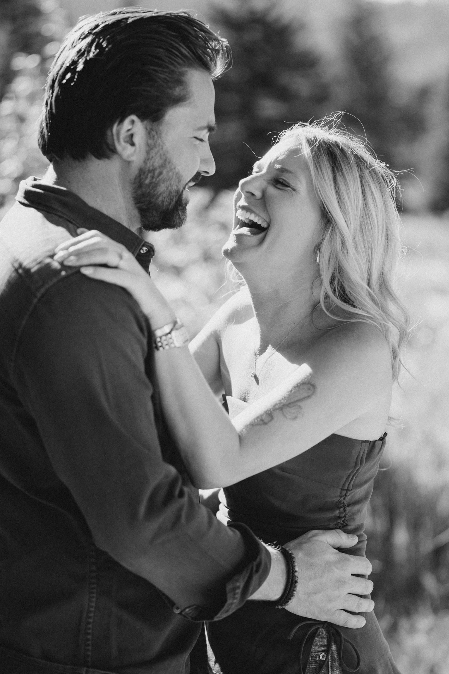 A romantic black and white portrait of a couple sharing a joyful laugh together outdoors.