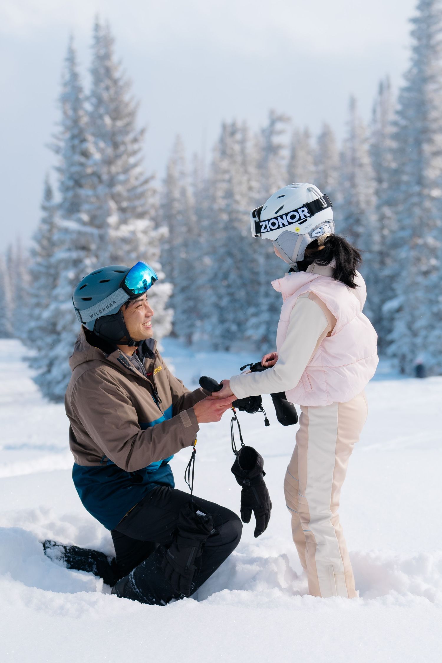 A photographer captures winter portraits in a snowy forest setting with evergreen trees in the background.