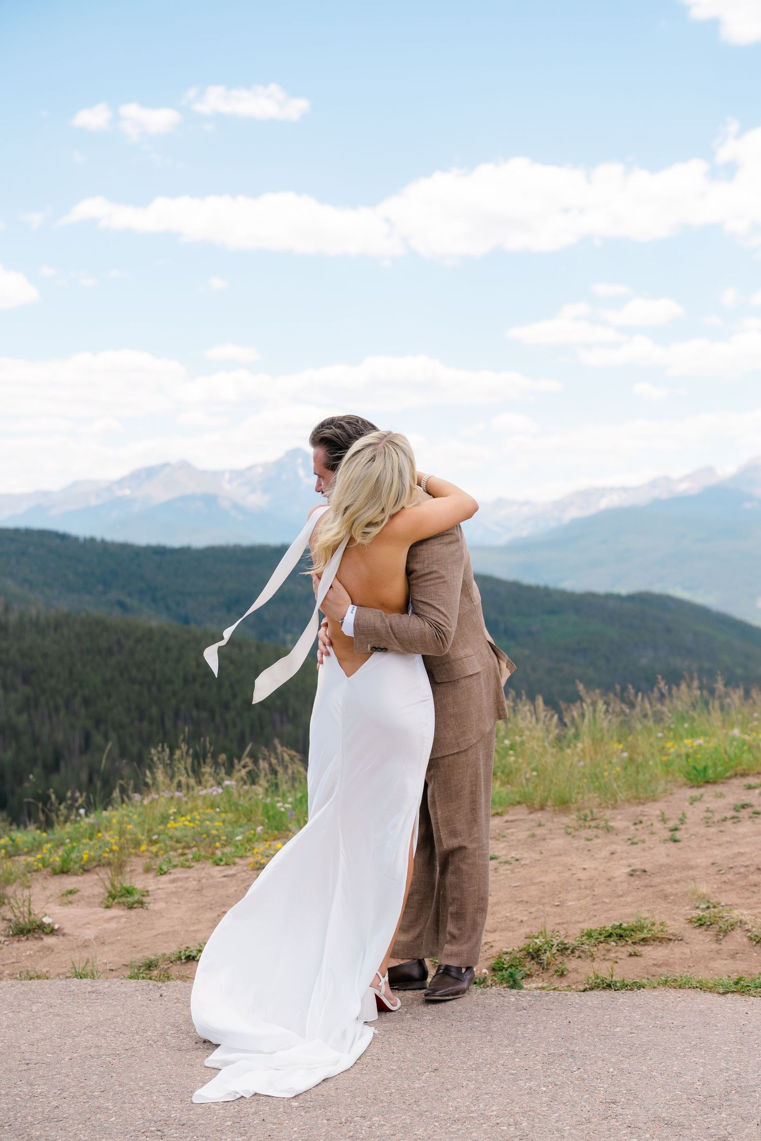 Bride and groom embrace with stunning mountain views behind them during outdoor wedding ceremony in Colorado.