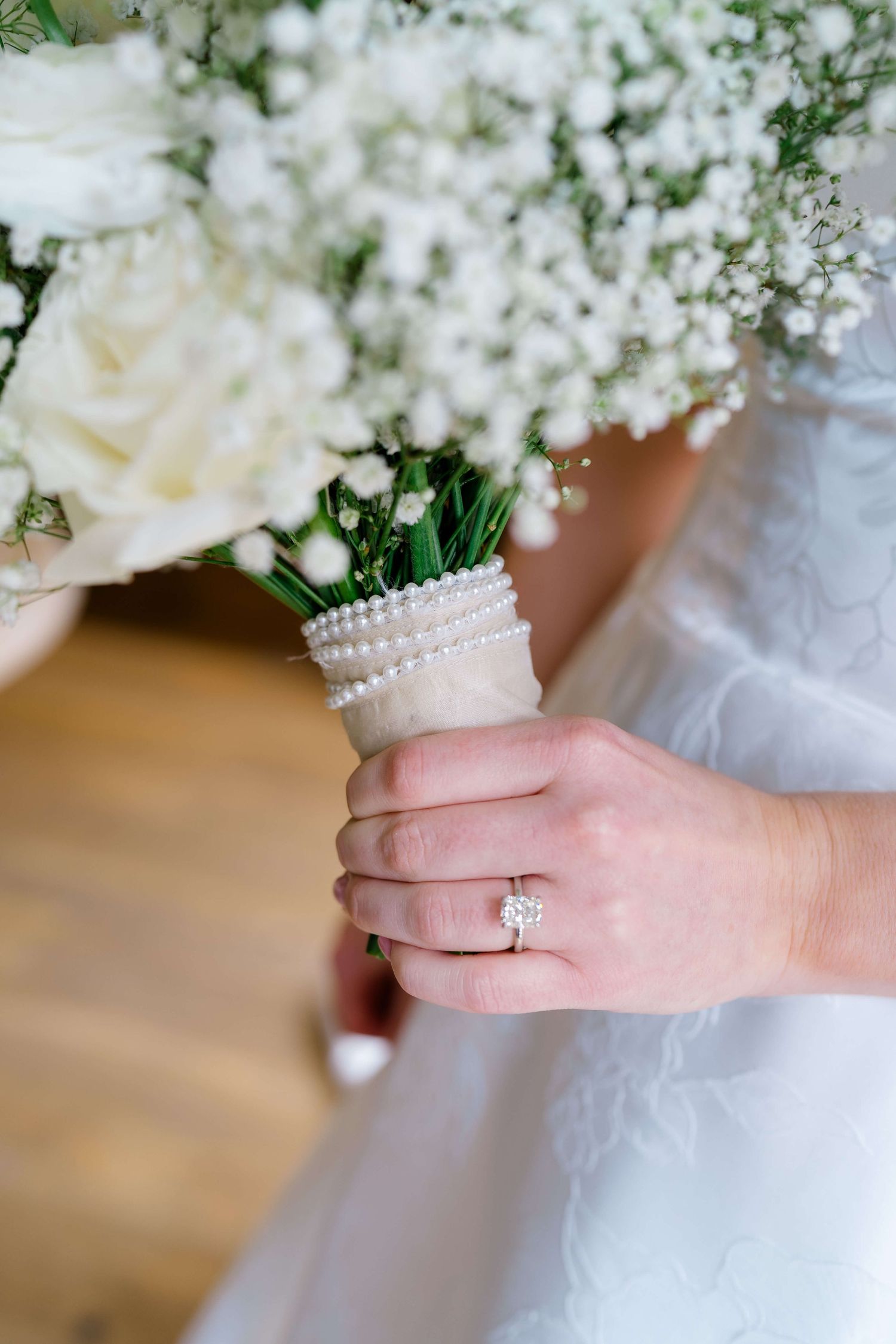Bride holding white rose and baby's breath bouquet with pearl handle wrap, showcasing diamond engagement ring on at Vail Sonnenalp Wedding.
