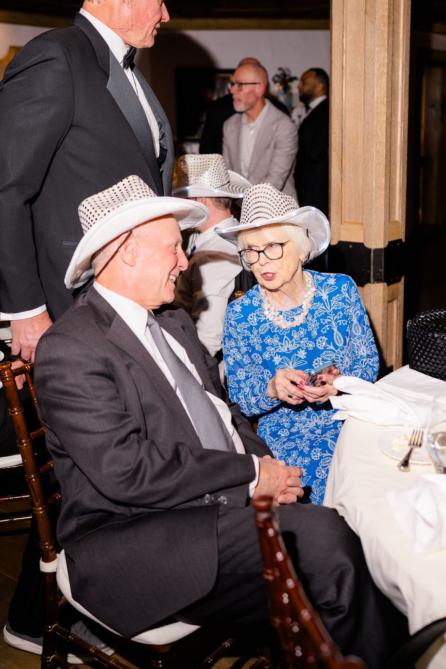 Elderly couple in white cowboy hats at a formal event, woman in blue floral dress with glasses at Vail Sonnenalp Wedding.