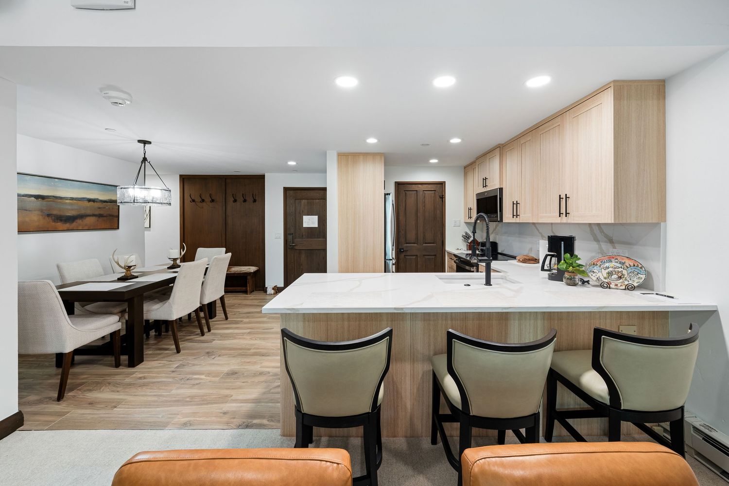 Modern kitchen with light wood cabinets, marble island, bar seating, and open dining area with pendant lighting.