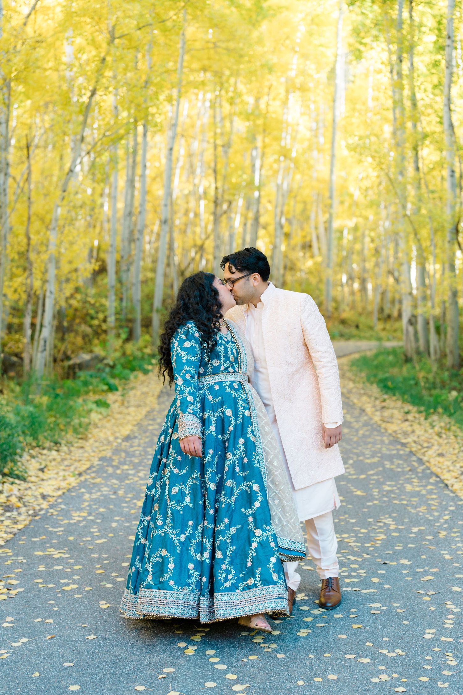 A couple in formal attire walk along a path surrounded by golden autumn aspen trees on a romantic afternoon.