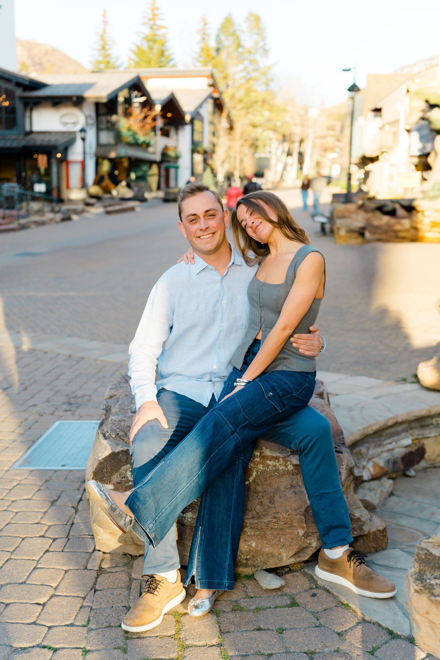 A couple sits together on stone steps in a charming village square during golden hour.