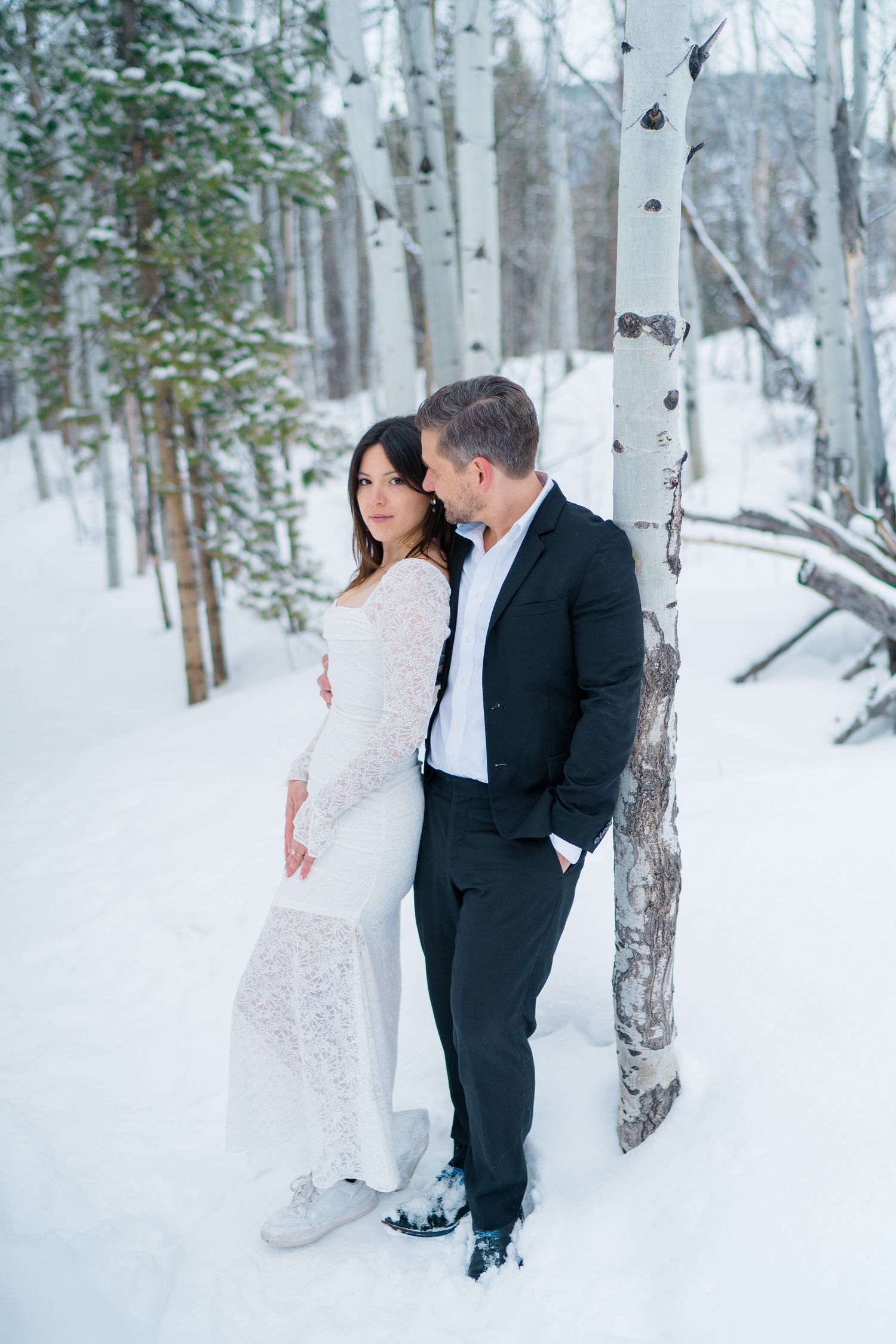A couple shares romantic moments in a snowy winter forest with white birch trees surrounding them.