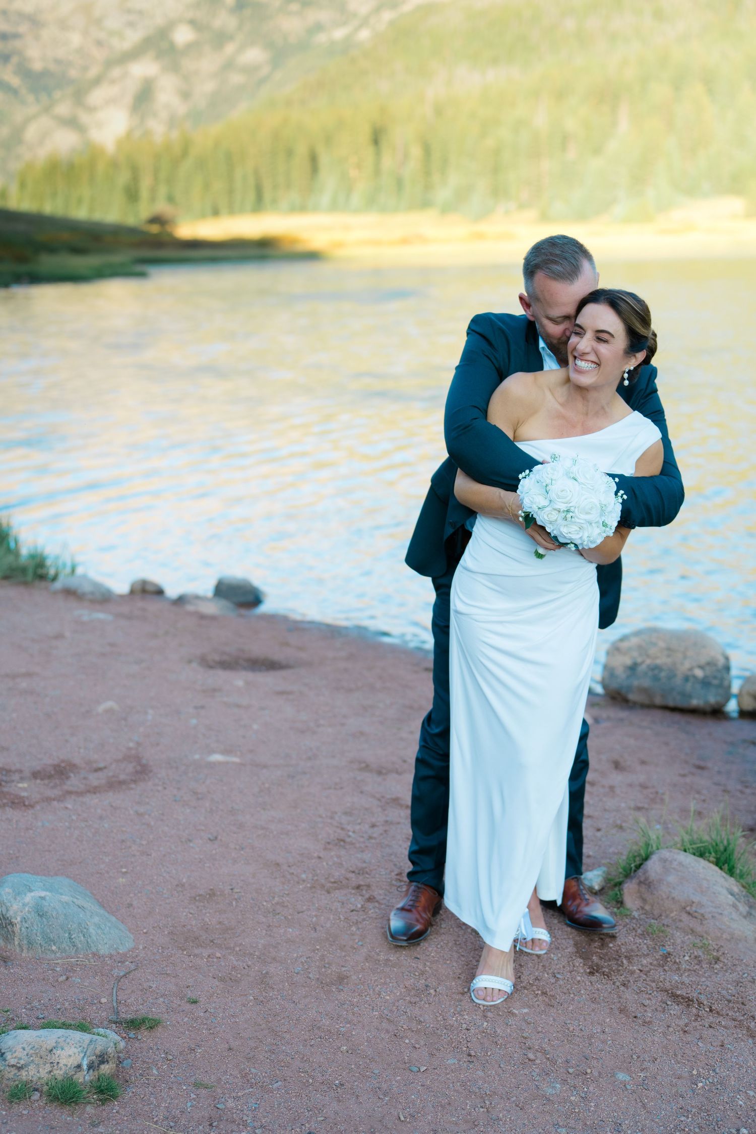 bride and groom laughing in front of lake