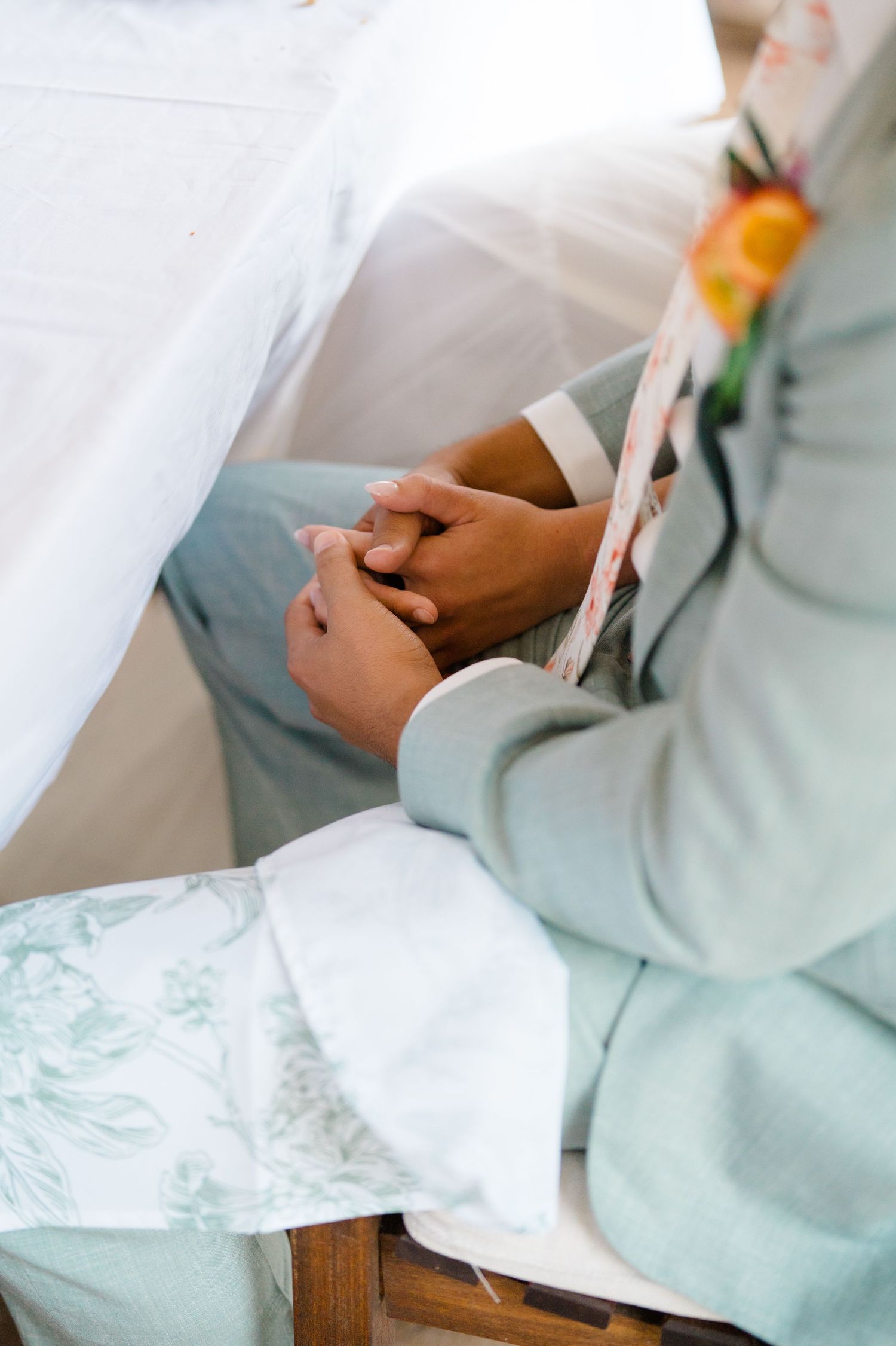 Close-up details of a mint green suit jacket and flowing white wedding dress fabric against a wooden surface.