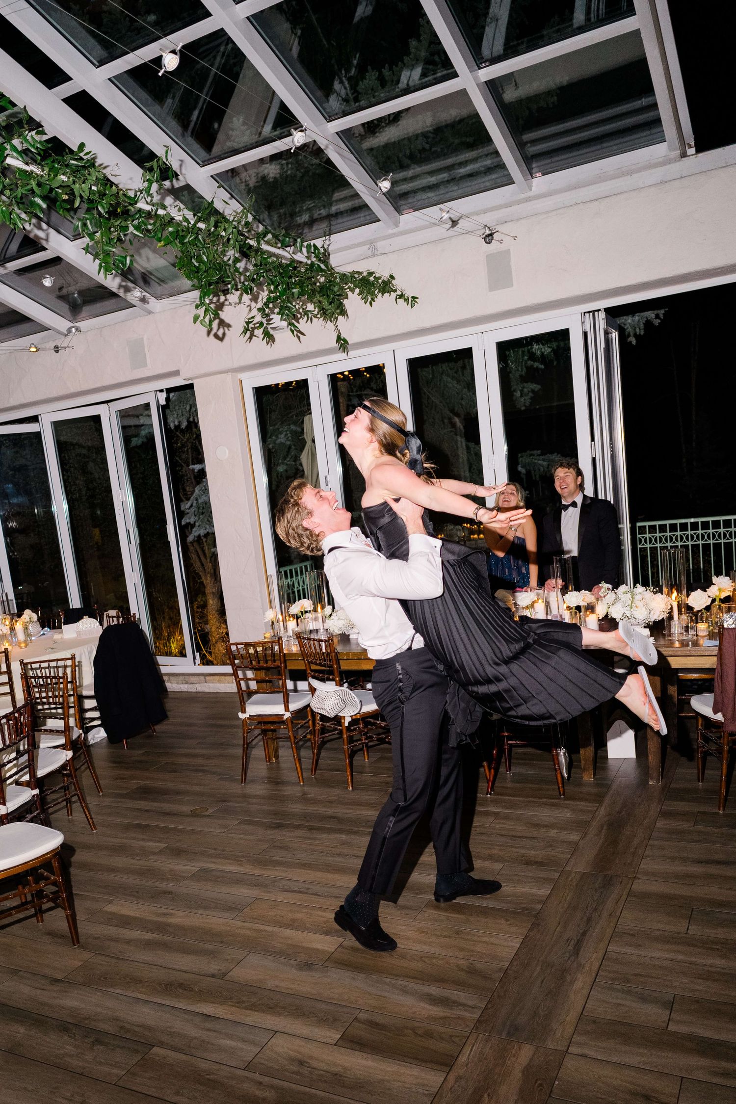 Couple sharing a dramatic dance lift on the floor of an elegant glass-ceiling reception venue at night.