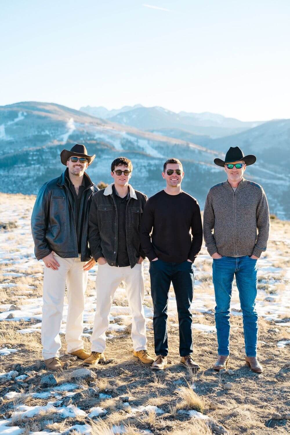 Four people in casual winter attire stand together against a snowy mountain backdrop in a panoramic photo series.