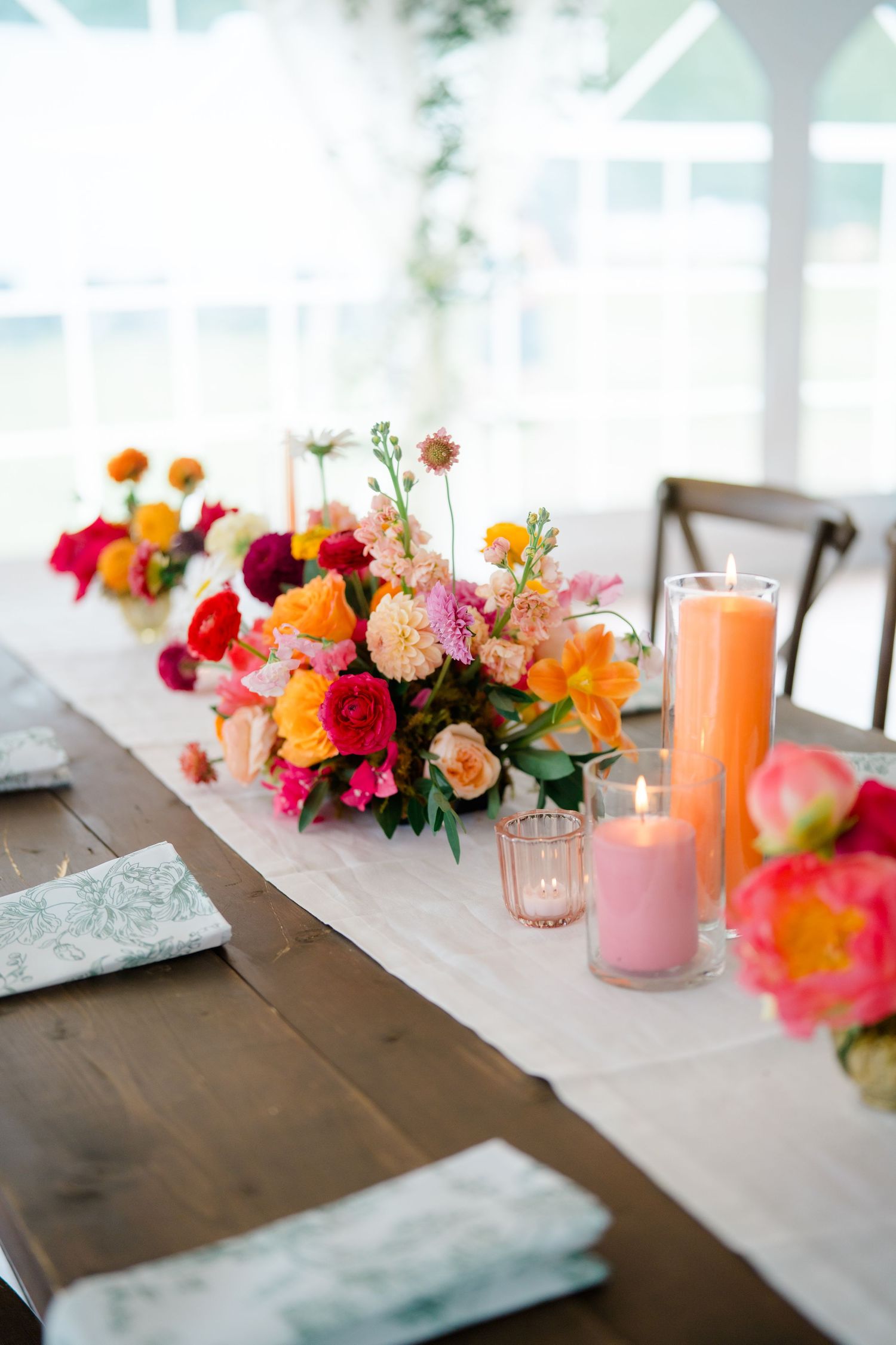 Elegant wedding reception table decorated with colorful floral centerpieces and pink and orange candles on a rustic wood surface.