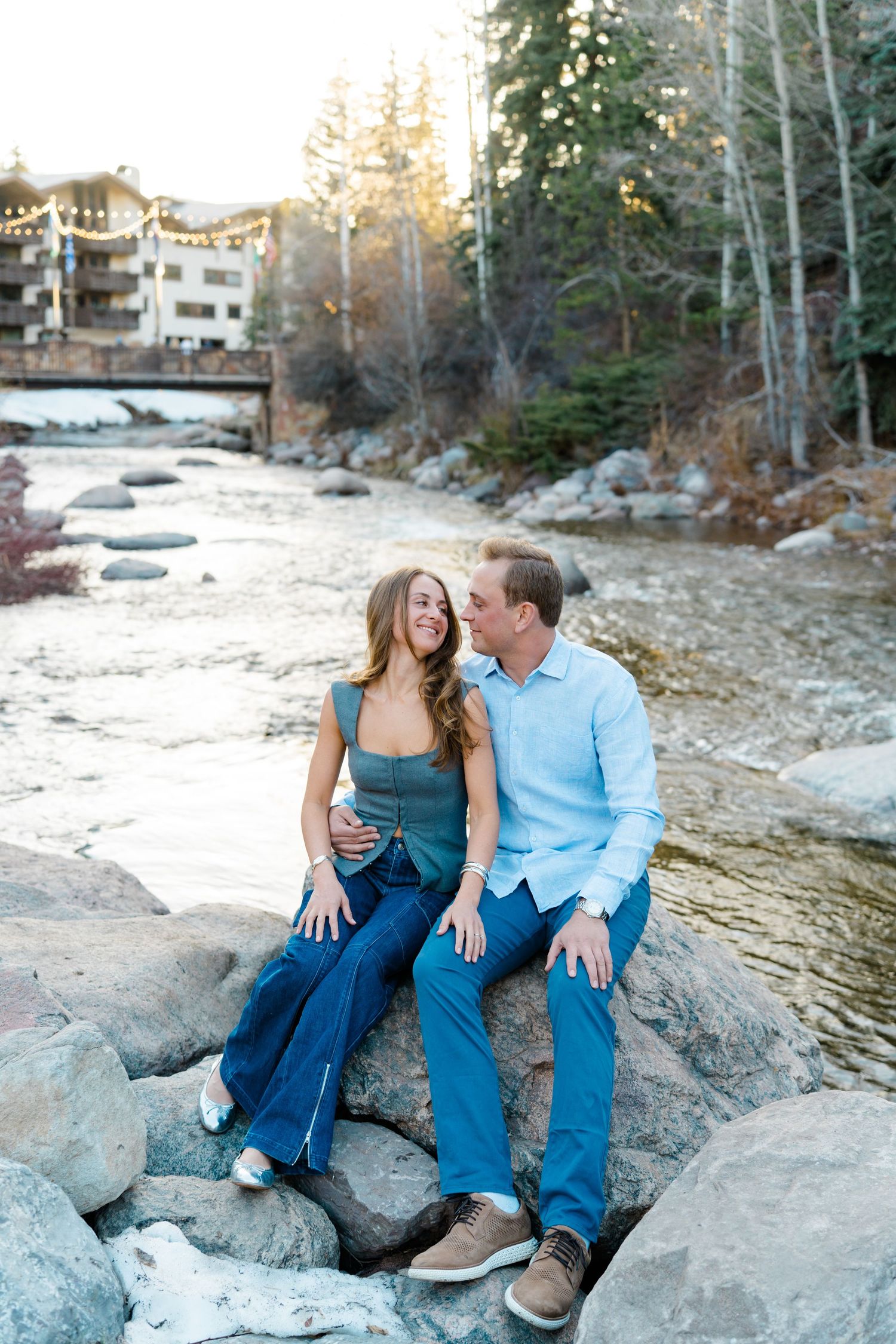 A couple sits together on rocky terrain during sunset in casual attire sharing intimate moments.