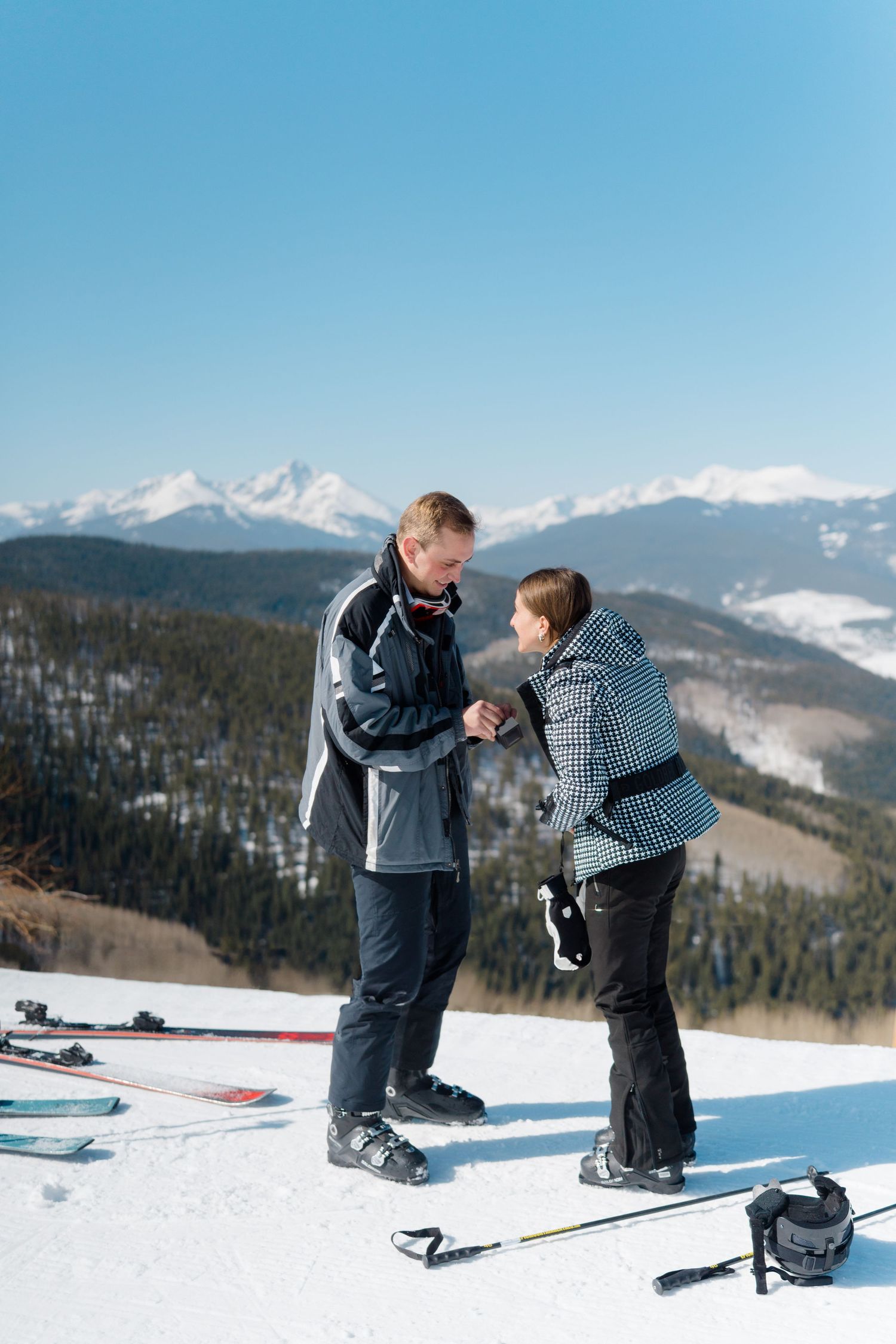 A romantic proposal scene unfolds on a snowy mountain slope with skis and winter gear.