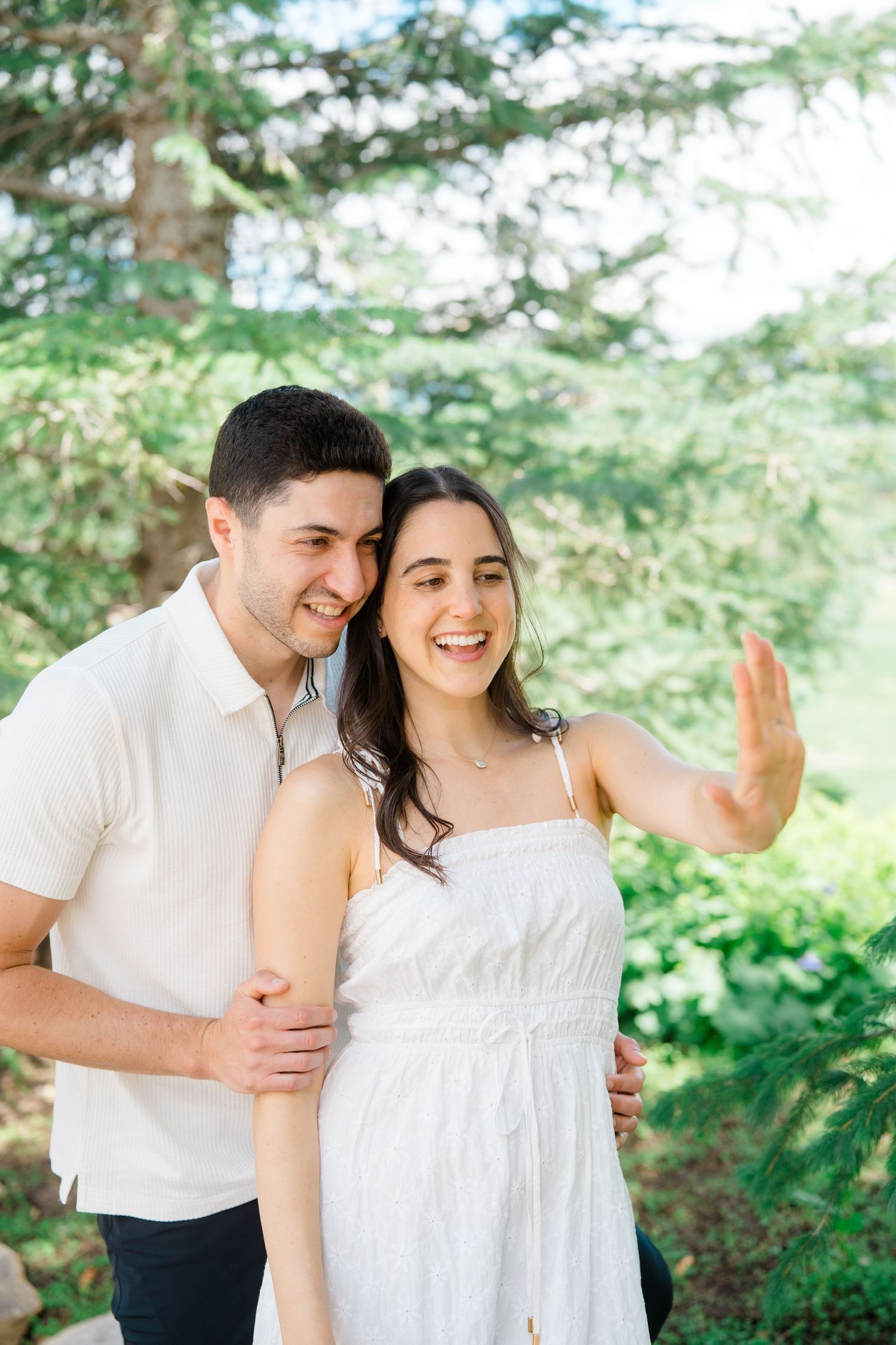 A couple shares intimate moments together outdoors among evergreen trees in coordinating white outfits.