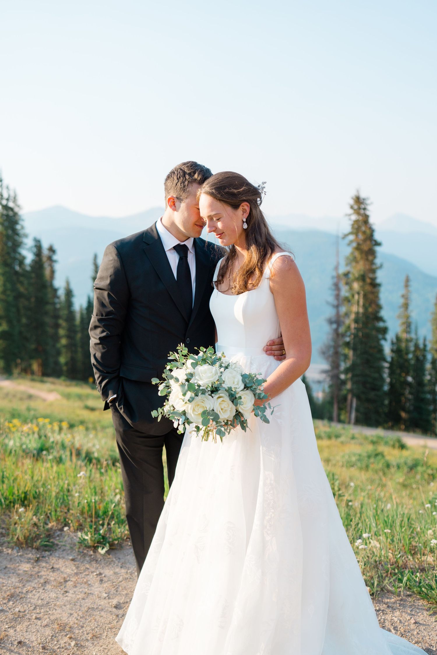 Romantic wedding couple embraces in a mountain meadow with white floral bouquet and scenic mountain backdrop at copper mountain.