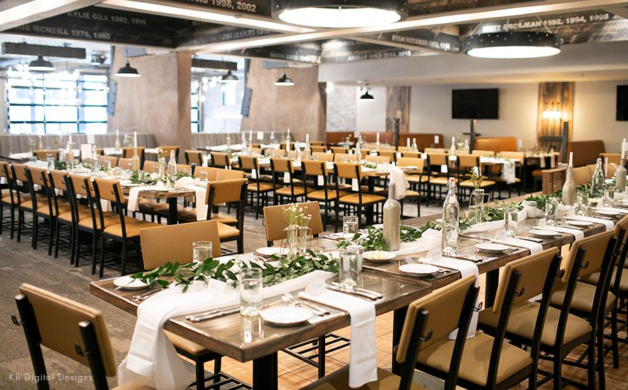 Elegant banquet hall with long tables set for a wedding reception with white linens and greenery.