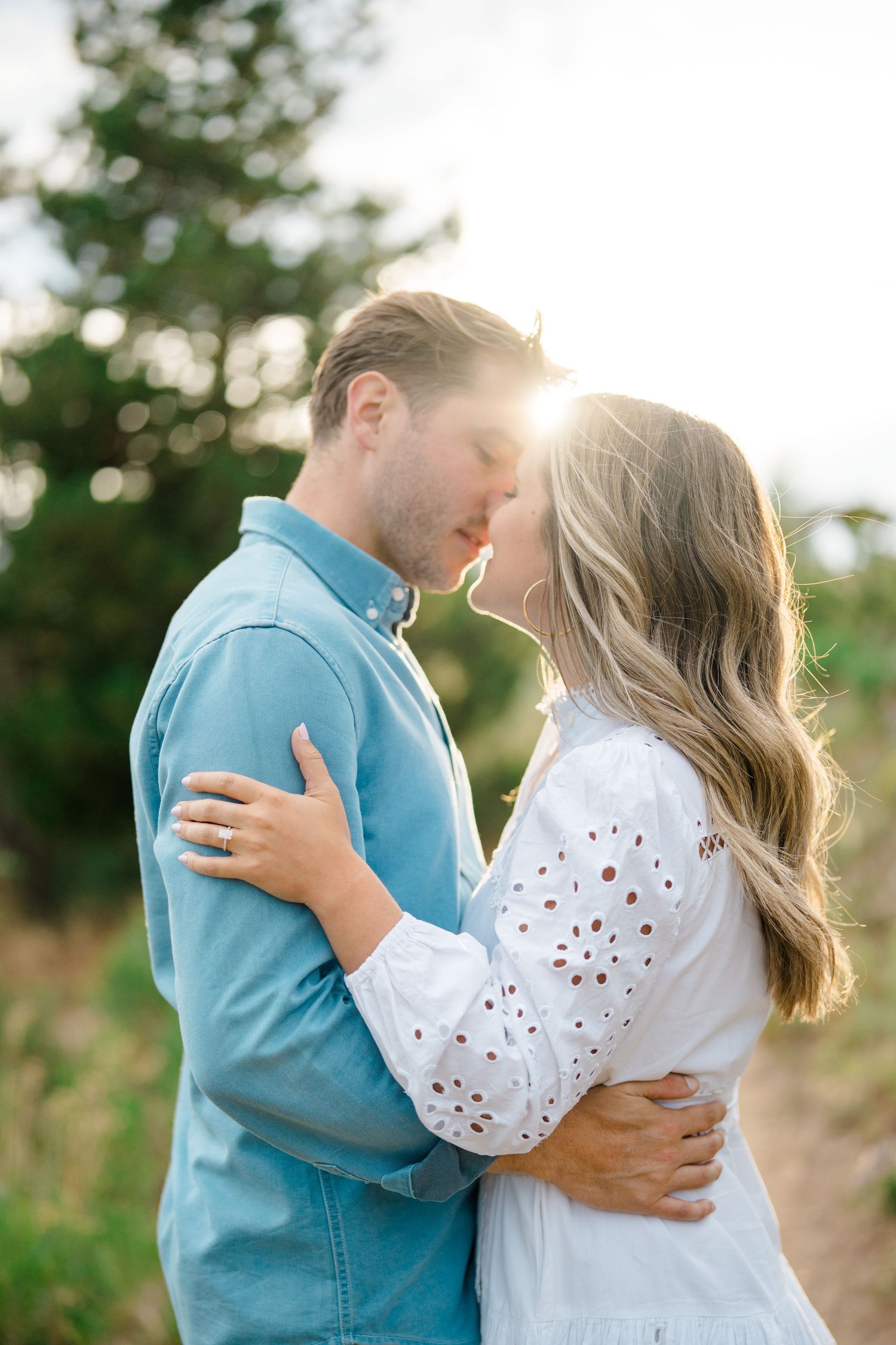 A romantic couple in blue and white clothing embraces during a golden sunset photoshoot in a natural outdoor setting at lake dillon.