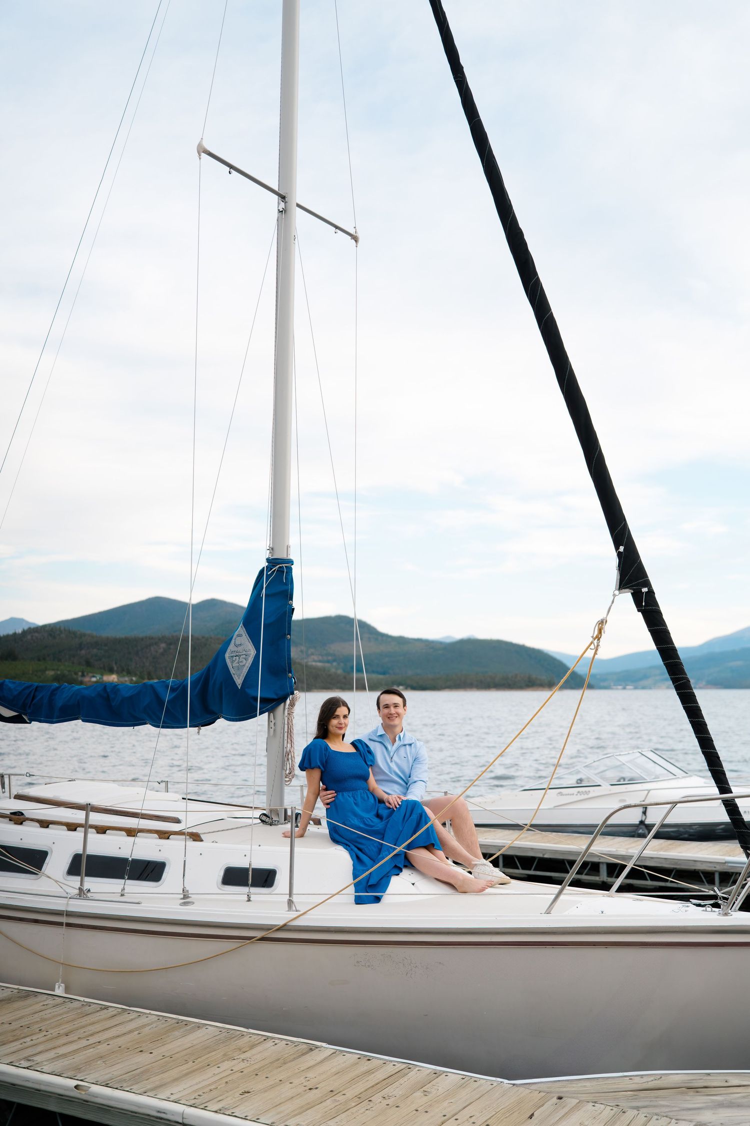 A series of white sailboats docked at a marina with mountains and blue sky in the background.