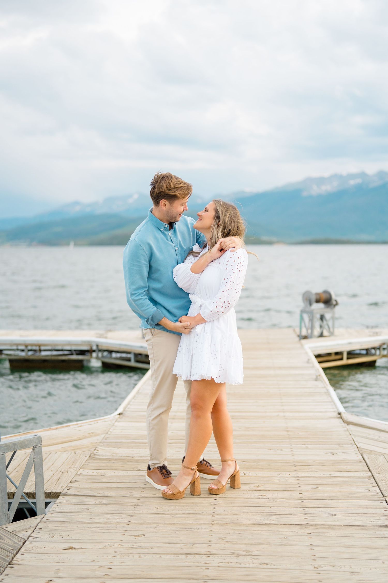 A couple shares an intimate moment on a wooden dock overlooking a mountain lake.