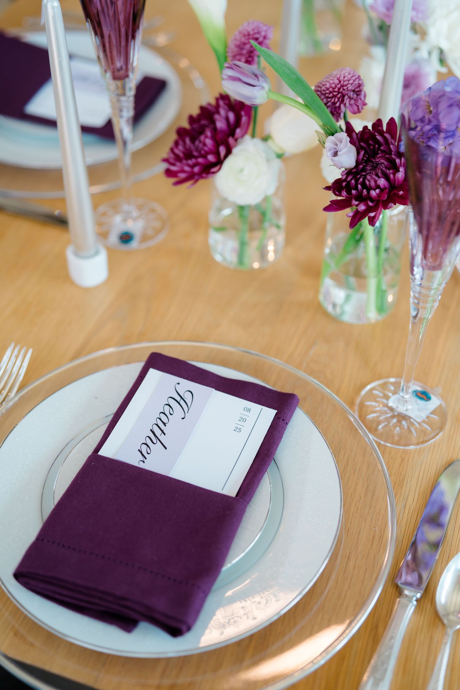 Elegant wedding table setting with purple napkins and floral centerpieces in glass vases.