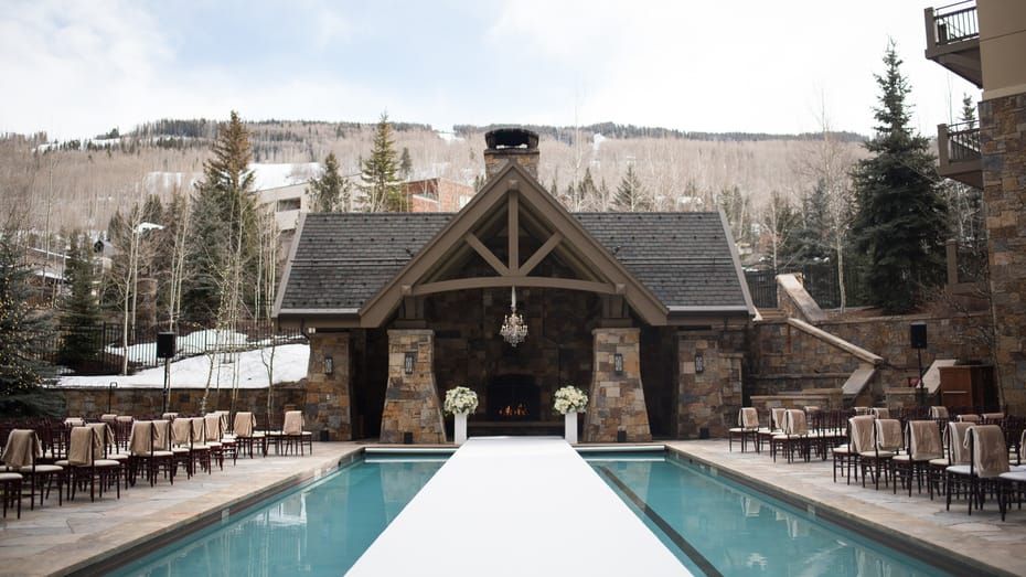 Elegant outdoor wedding ceremony setup beside a pool with rustic lodge backdrop and snow-covered mountains in Vail, Colorado.