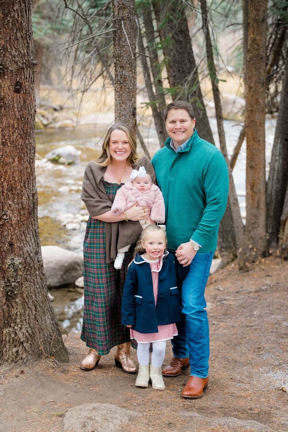 A family stands together in a wooded outdoor setting wearing coordinated casual outfits for a portrait session - best vail family locations