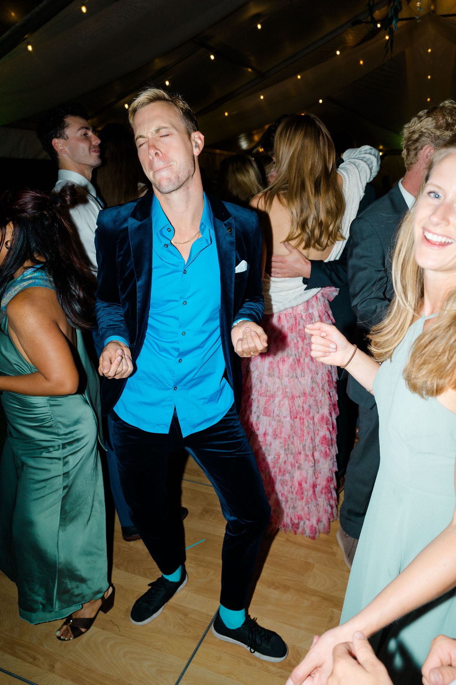 People dancing and having fun on a wooden dance floor at a party with twinkling lights overhead.