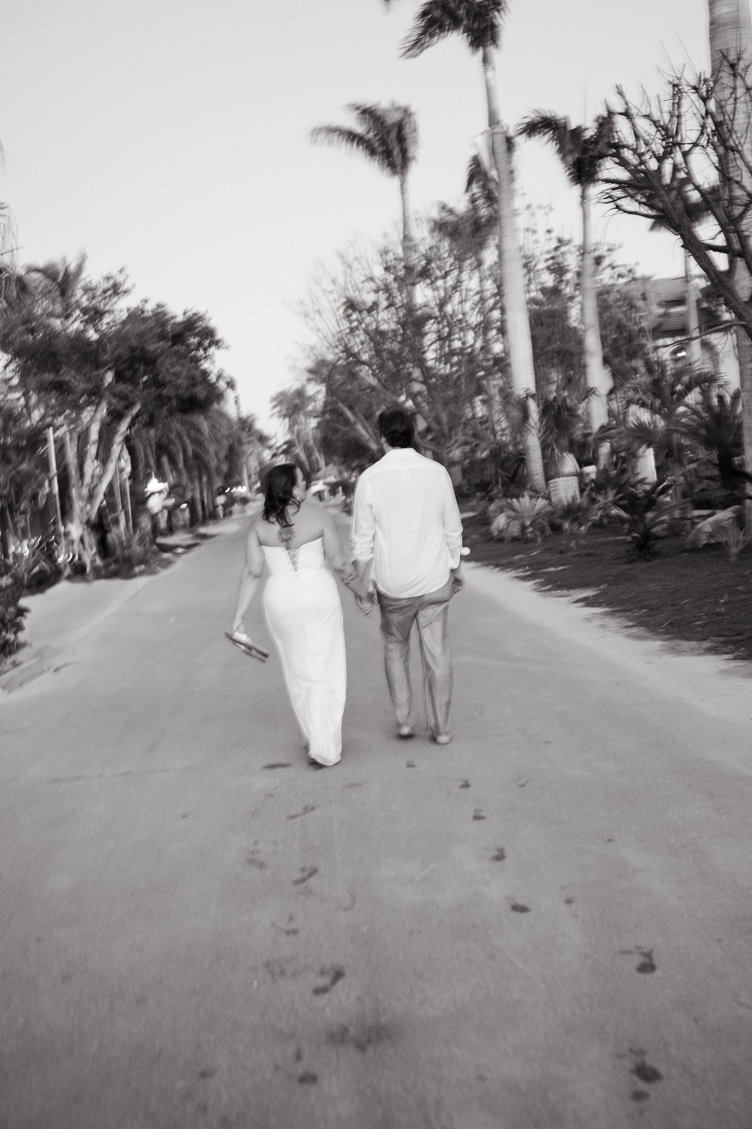 Black and white photo of palm-lined path with walking figures in distance.