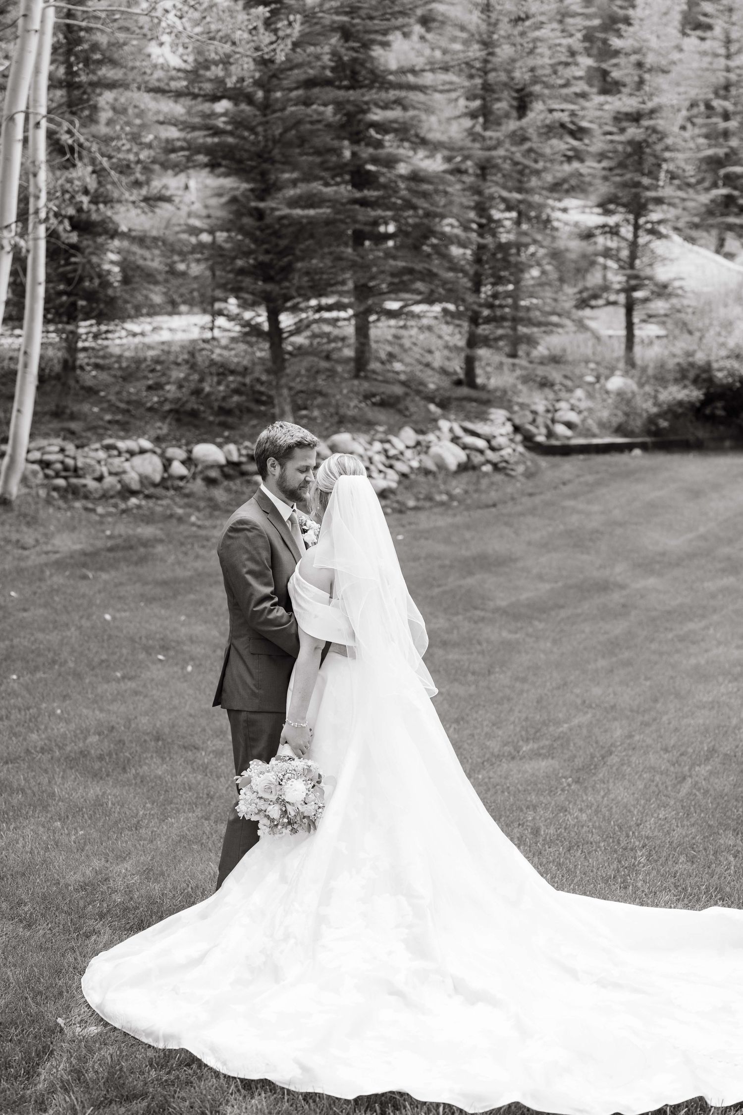 Vail Wedding Session - Black and white wedding portrait showing a flowing train on a grassy hillside with pine trees.