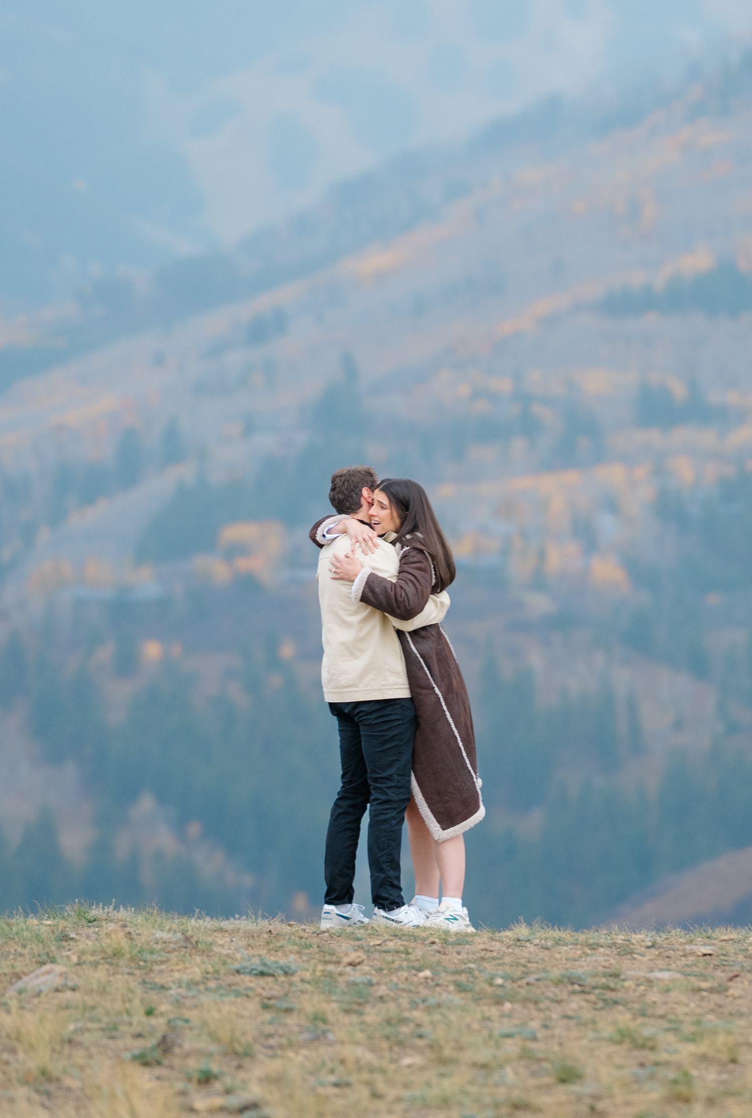 A couple embraces on a hilltop overlooking autumn mountains in a romantic moment.