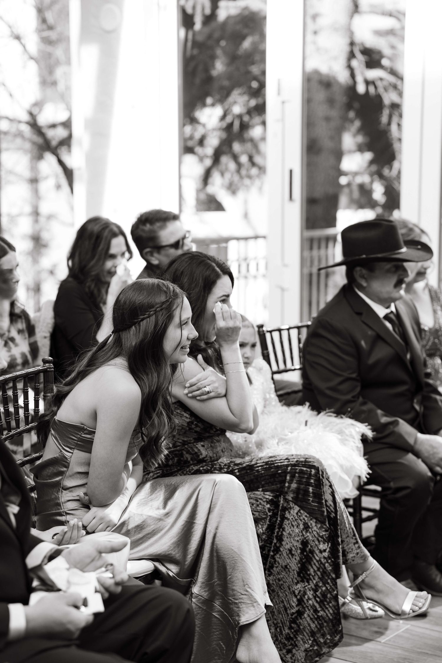 Emotional wedding guests wipe tears during outdoor ceremony in black and white photo.