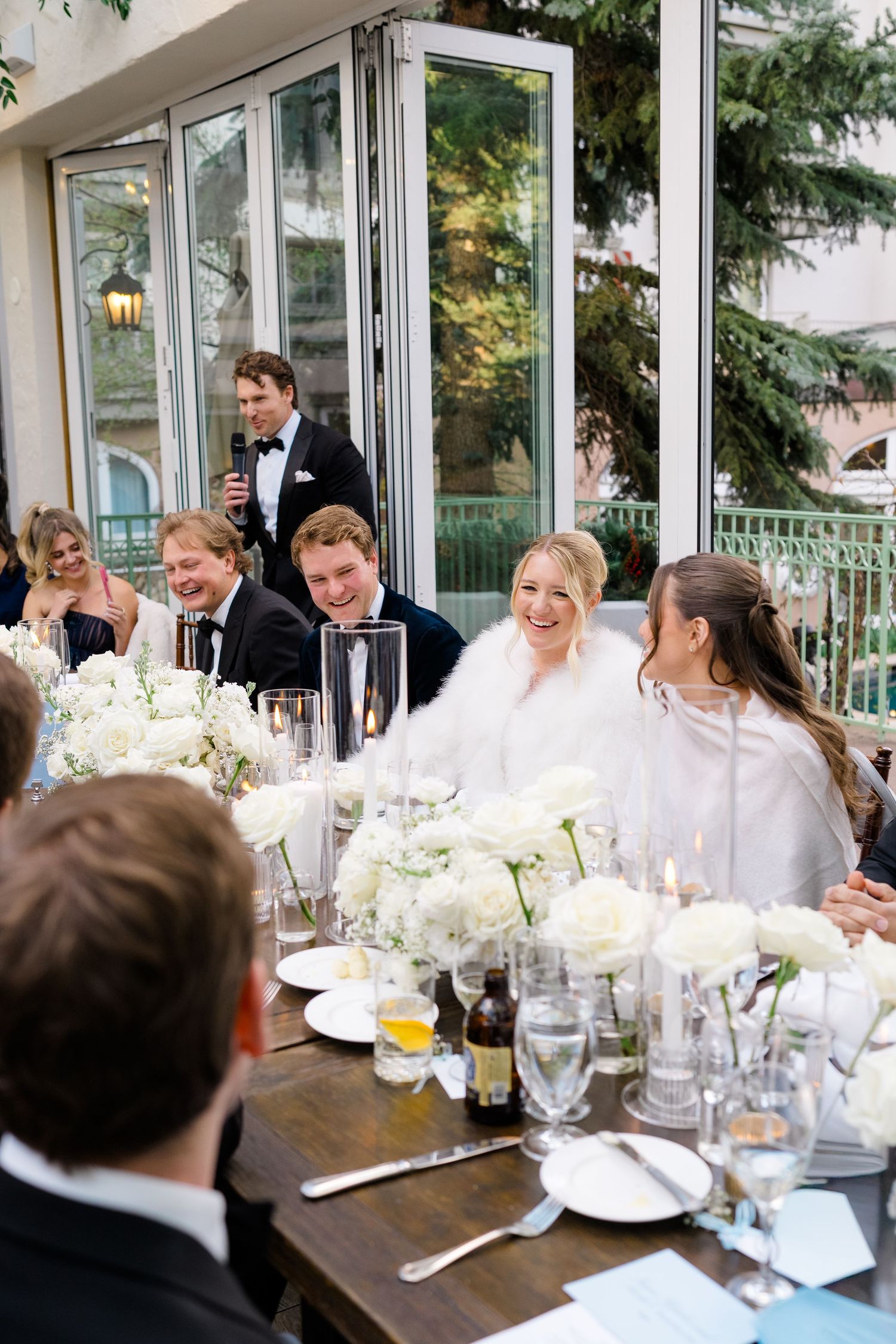 Bride laughing joyfully at wedding reception dinner table adorned with white floral centerpieces and elegant glassware at The Sonnenalp.