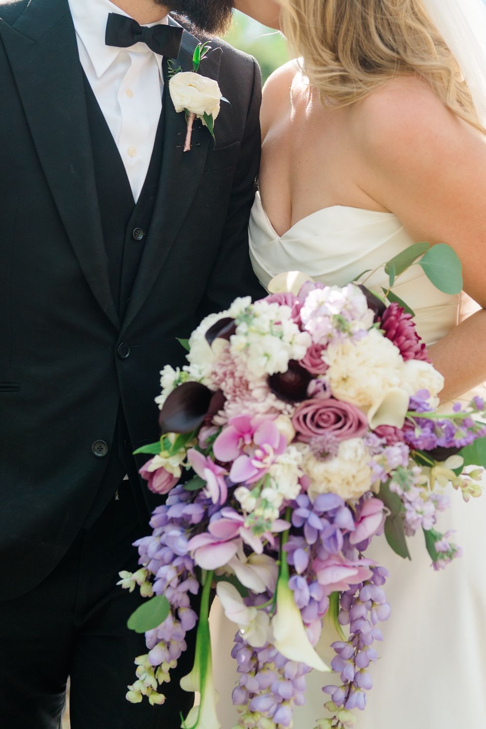 Cascading purple and white wedding bouquet with orchids and roses against a white wedding dress taken by breckenridge wedding photographer