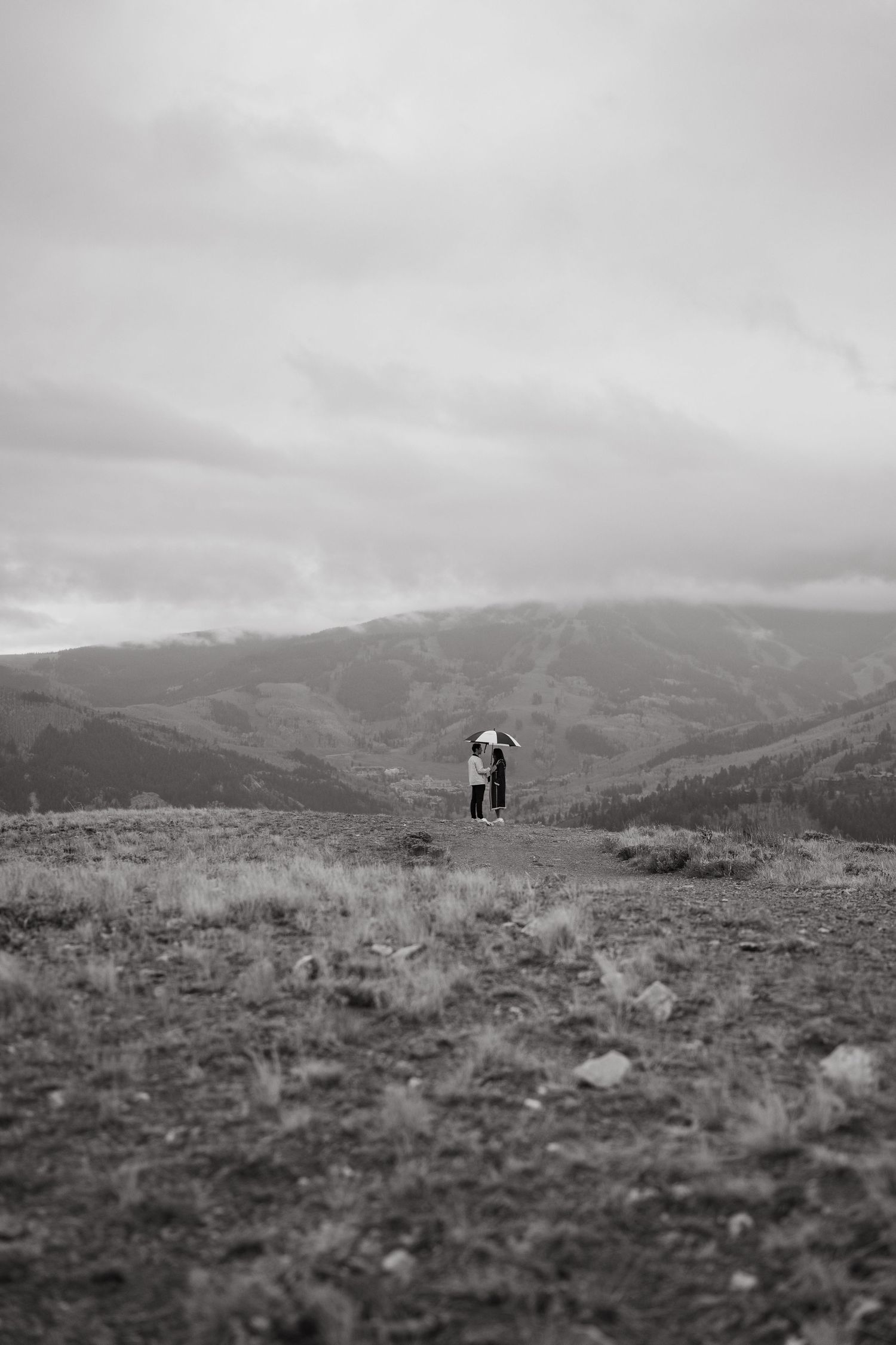 Black and white panoramic sequence shows two silhouettes walking on a hilltop against a dramatic mountainous landscape.
