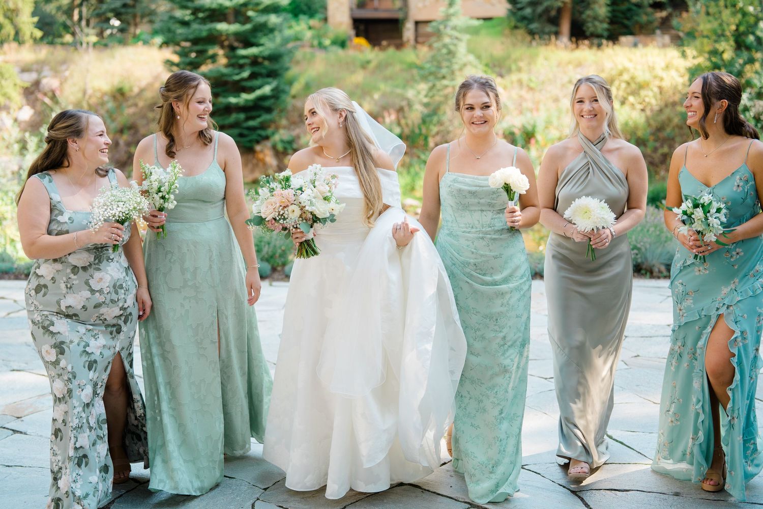 Bridesmaids in mint green dresses pose together outdoors at a summer wedding celebration.