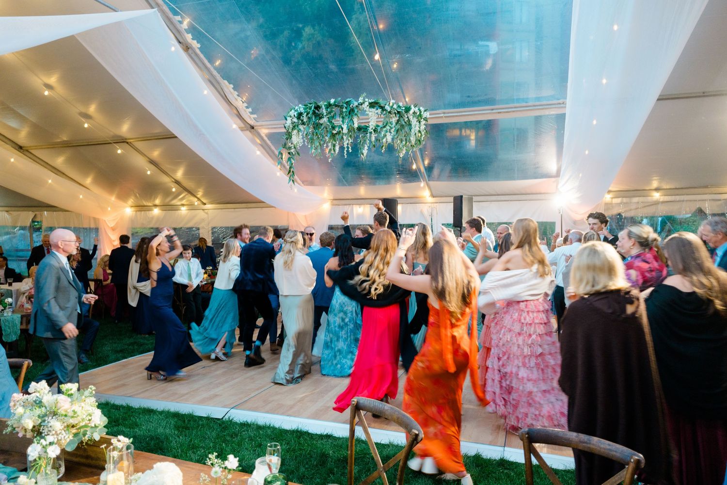 A panoramic view of a crowded indoor wedding reception with guests mingling under decorative lighting and floral arrangements.