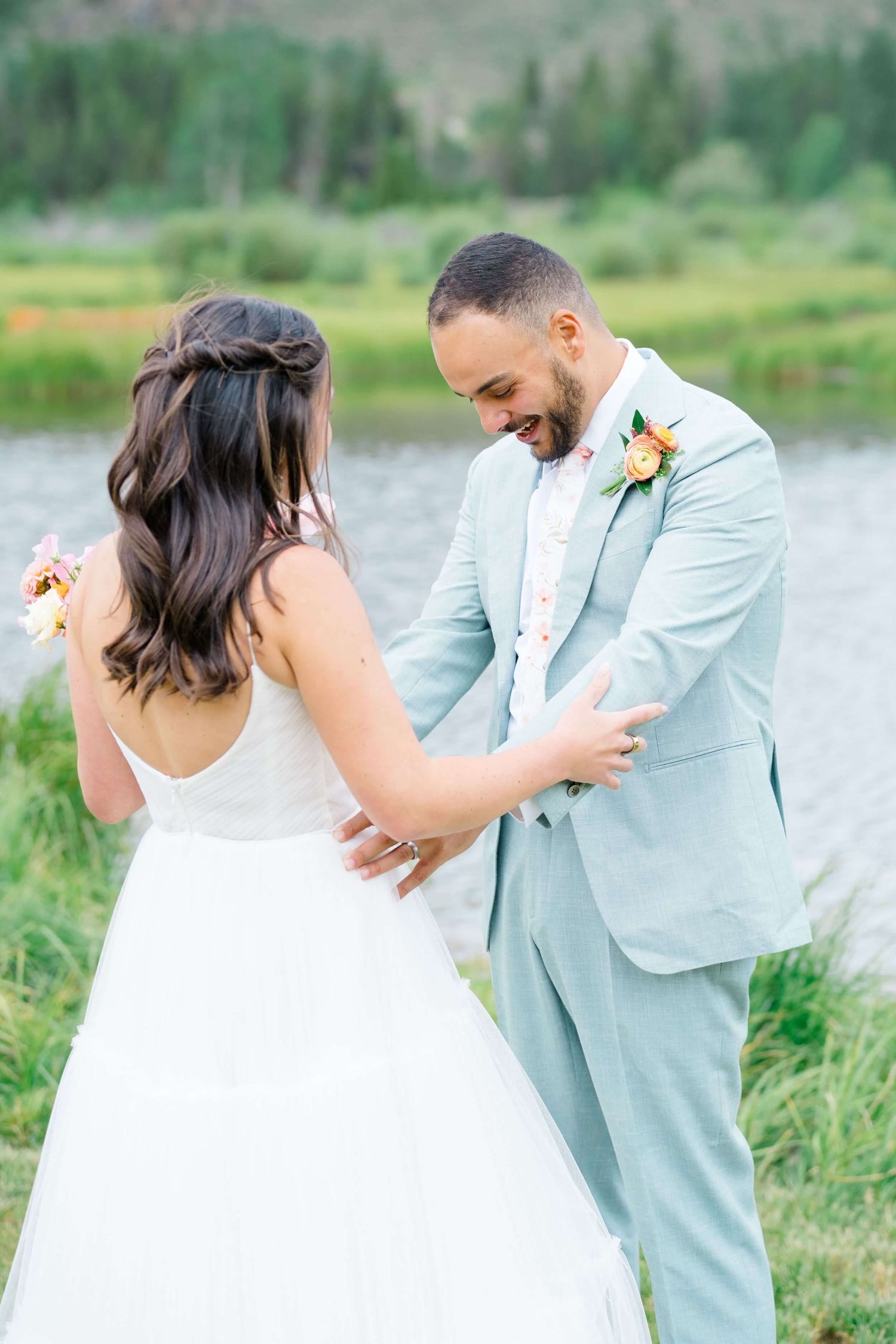 Intimate Camp Hale wedding moment captured by mountain lake with couple in white dress and light blue suit.