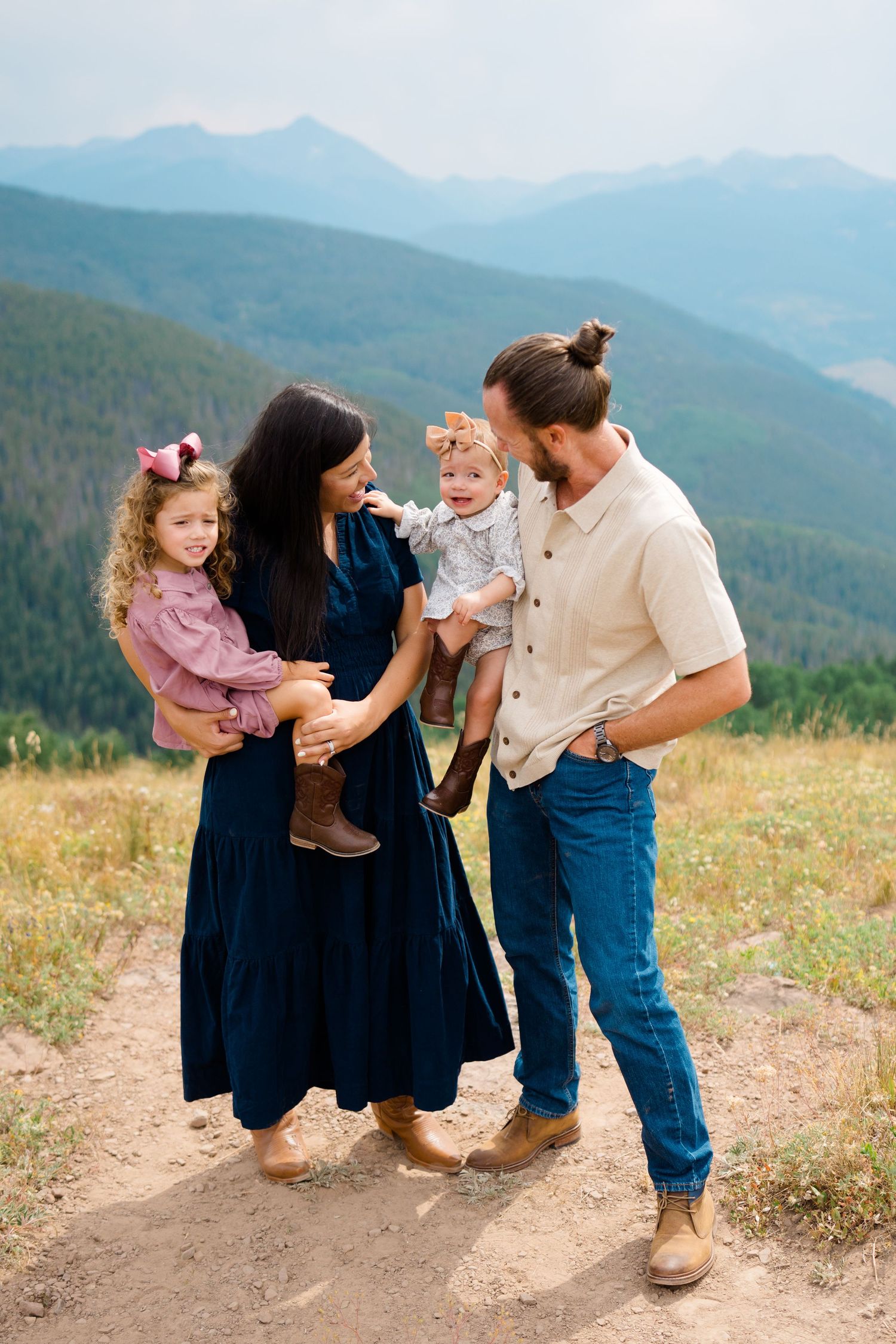 A family shares a joyful moment together on a mountain trail with scenic mountain ranges in the background during vail mountaintop session.
