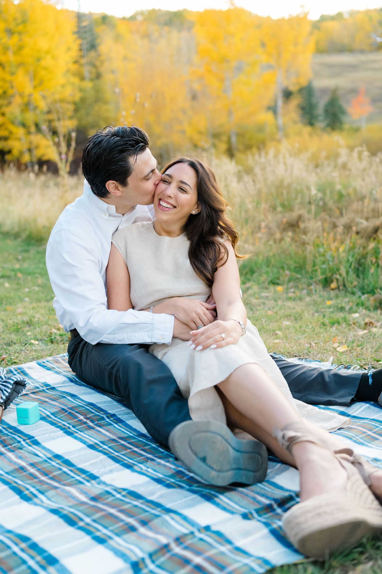 Couple sharing romantic moments on a plaid blanket with autumn foliage in the background.
