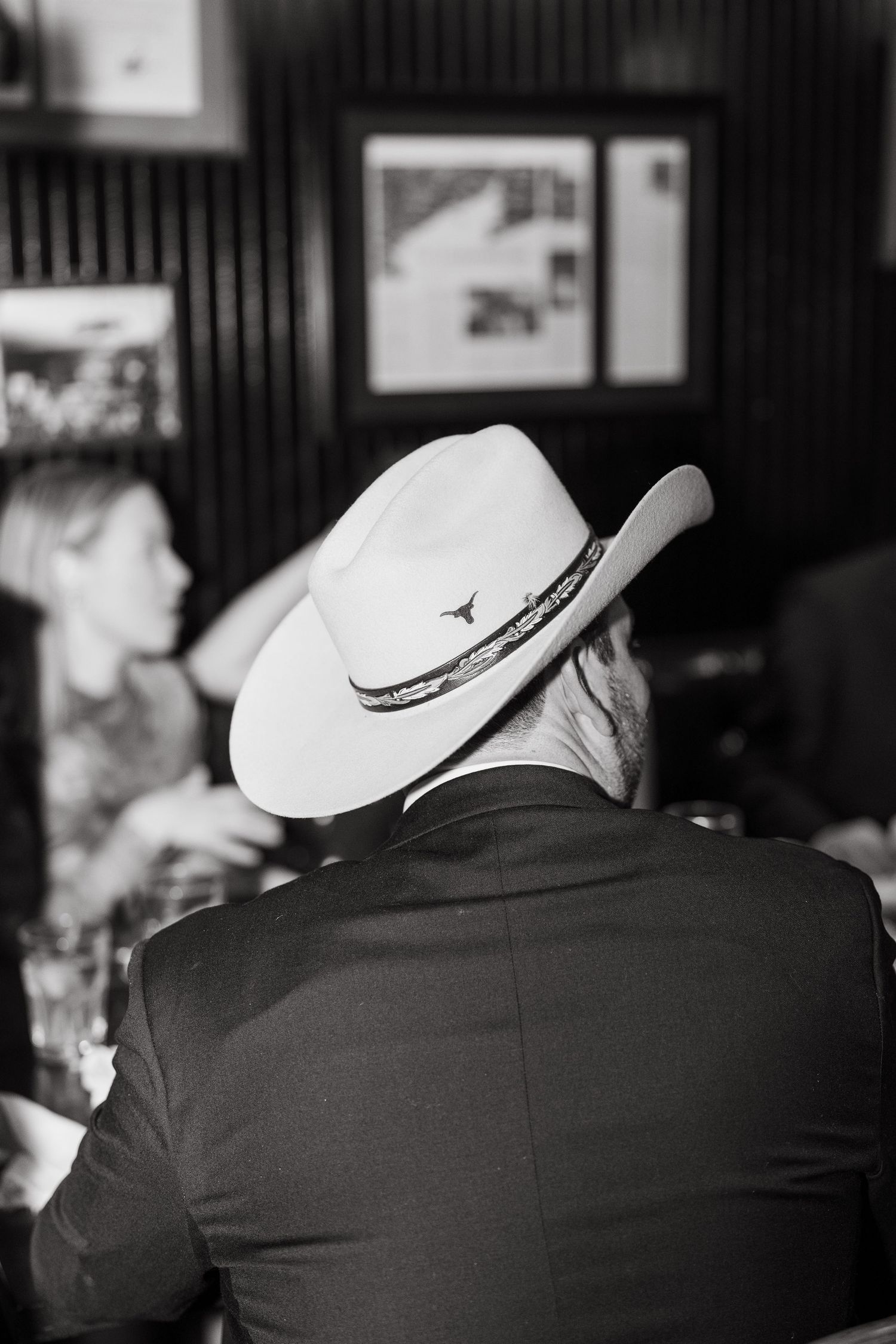 Row of men wearing cowboy hats and dark suits shown from behind at a formal event.