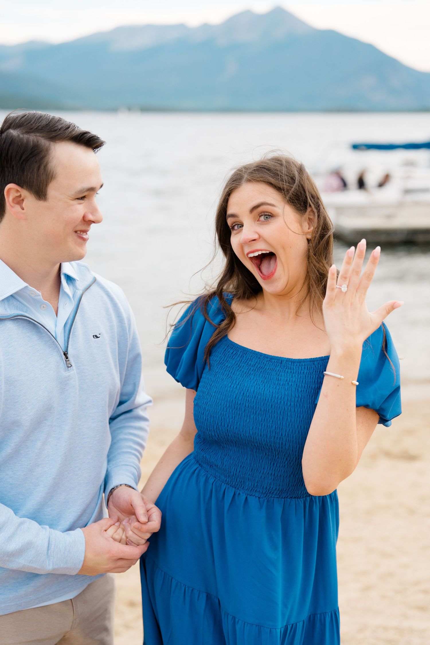 A couple shares a joyful moment together on a beach with mountains visible in the background after surprise proposal at lake dillon.